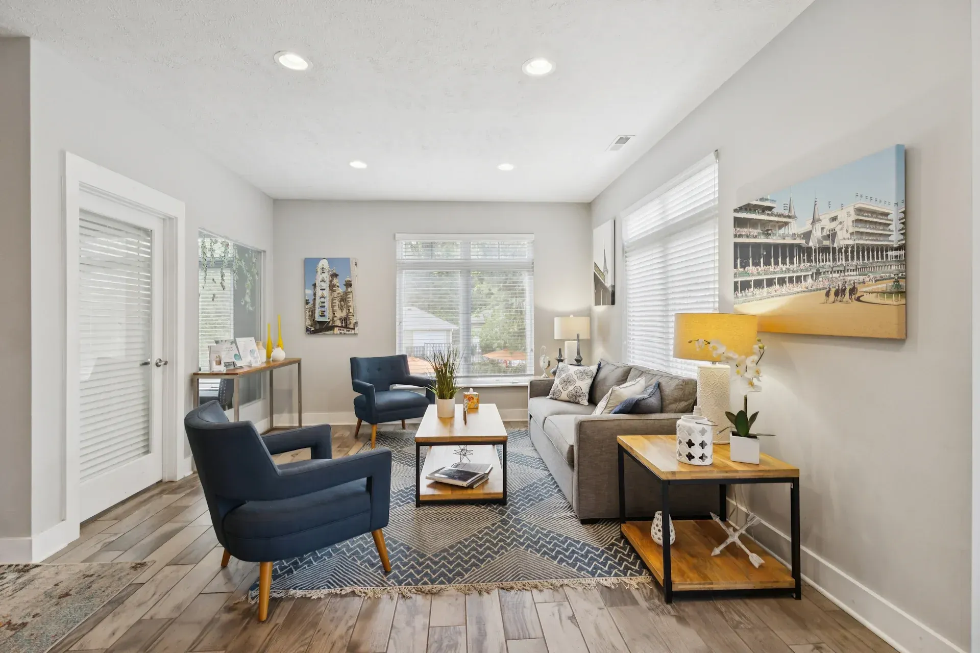 Living room with blue armchairs, gray sofa, wooden tables, and artwork on gray walls.