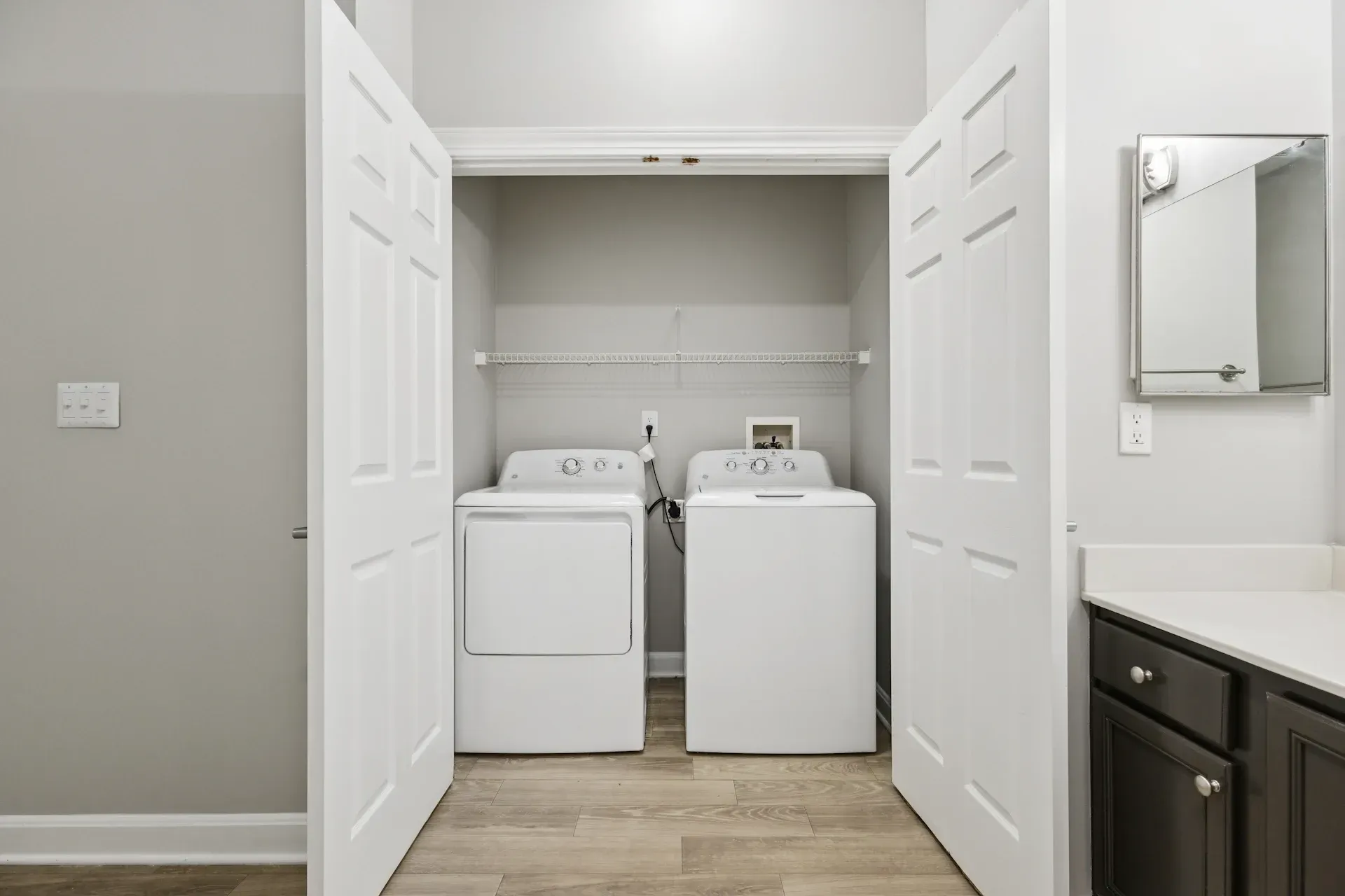 Laundry closet with white washer and dryer, open doors, and a small shelf.