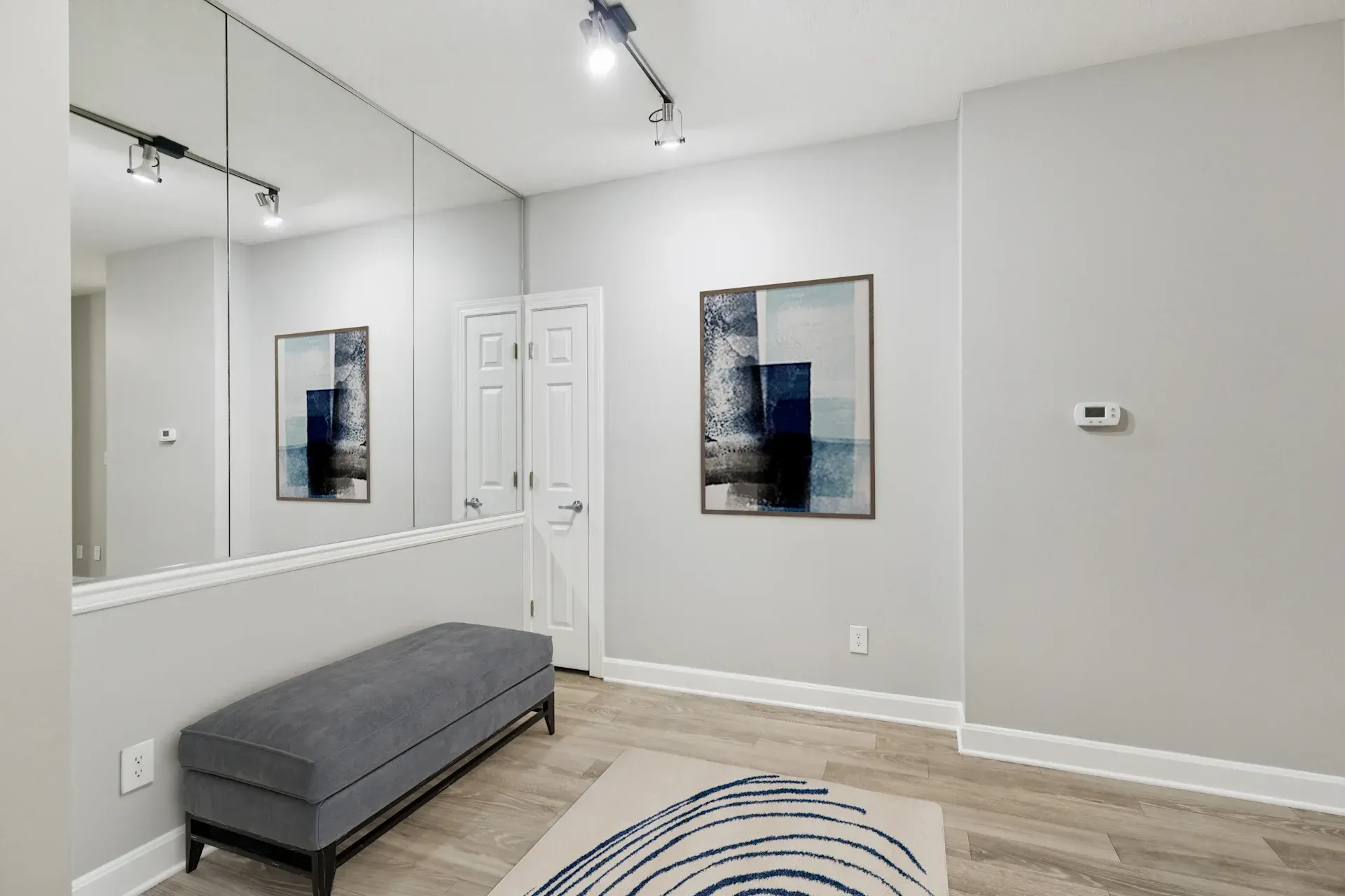 Hallway with a bench, abstract art, a large mirror, and track lighting.