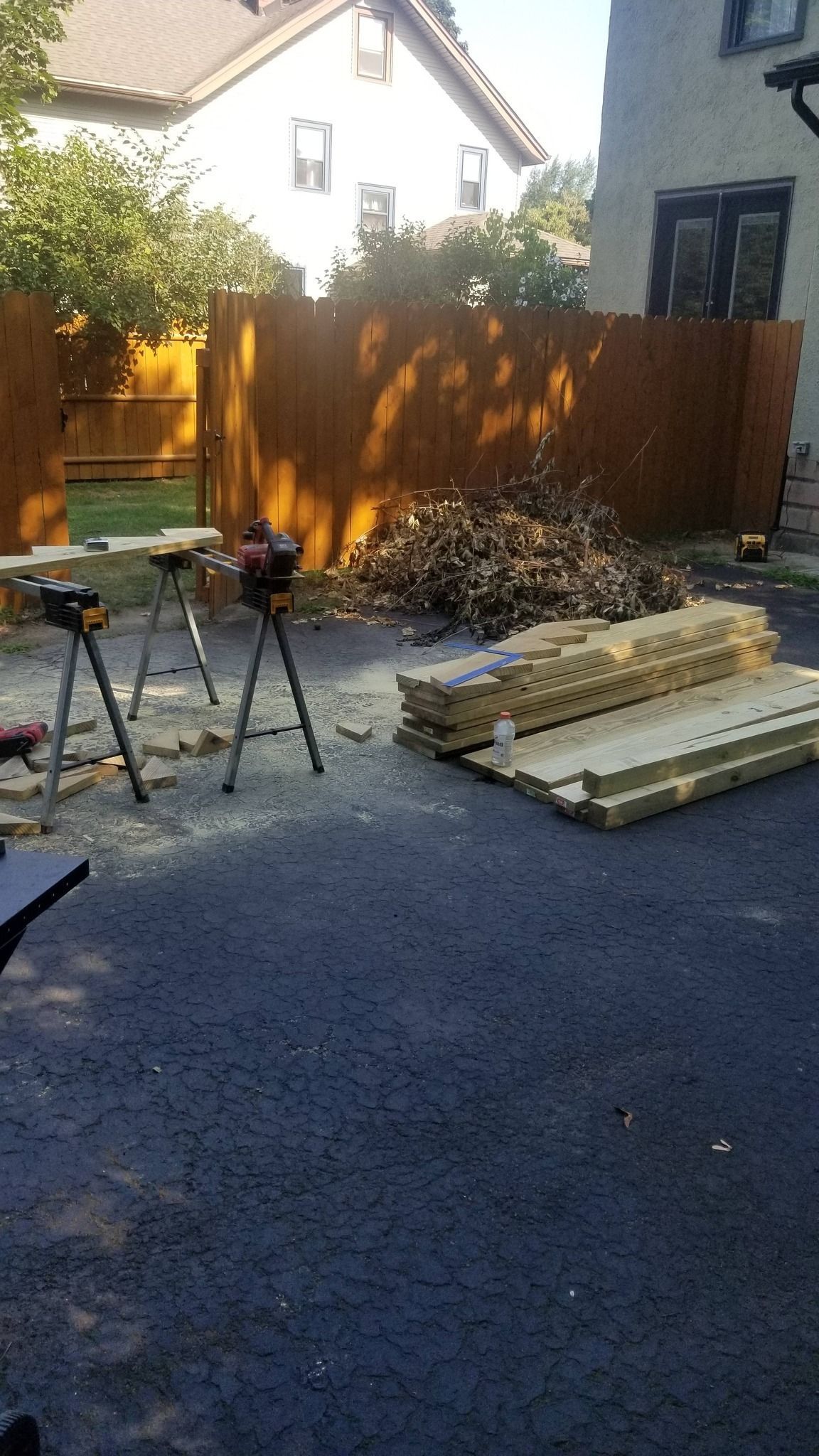 Backyard with lumber stacks, tools on tripods, and a wood fence in sunlight