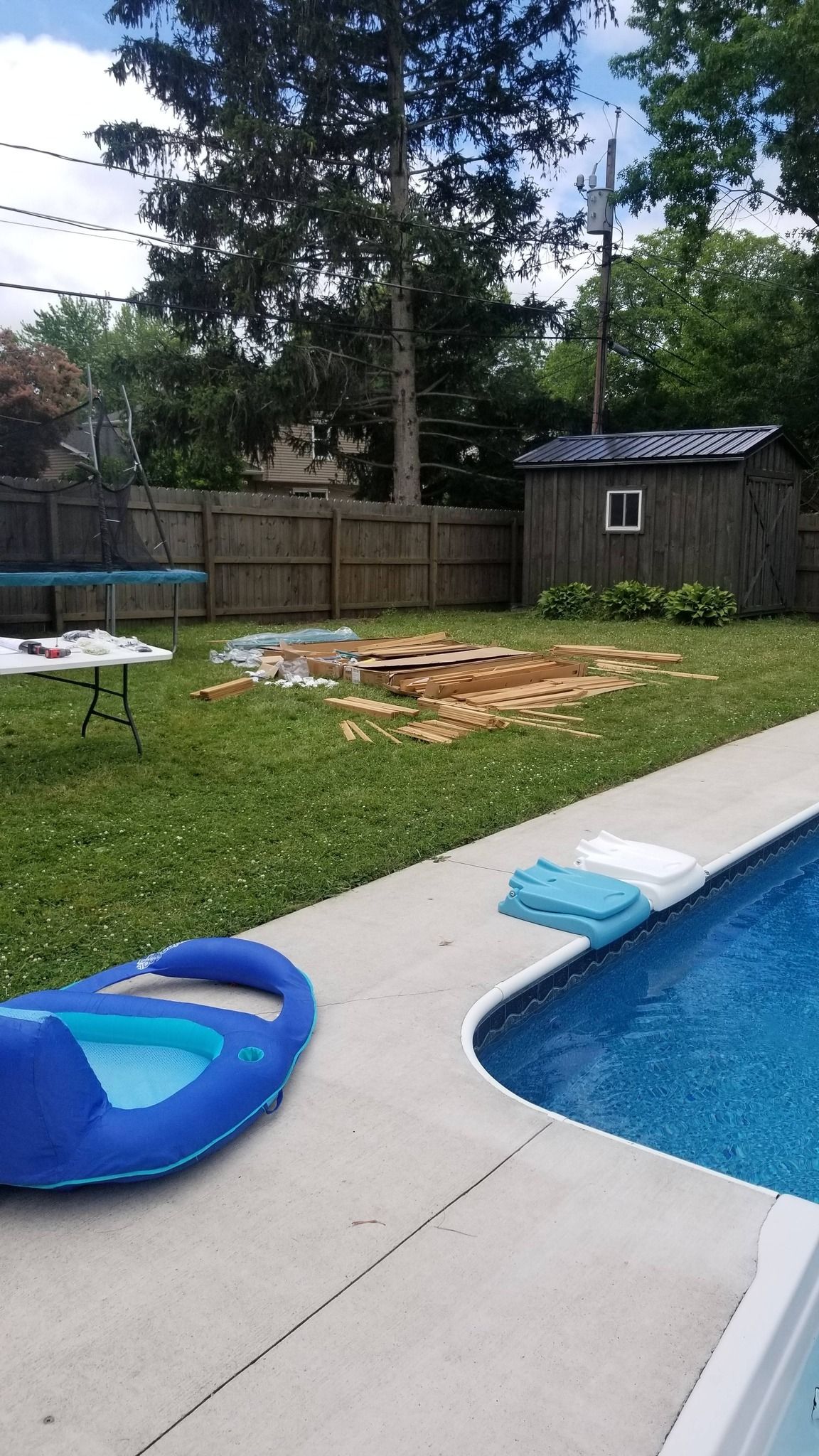 Backyard with a swimming pool, blue float, lawn, wooden fence, and small shed under trees