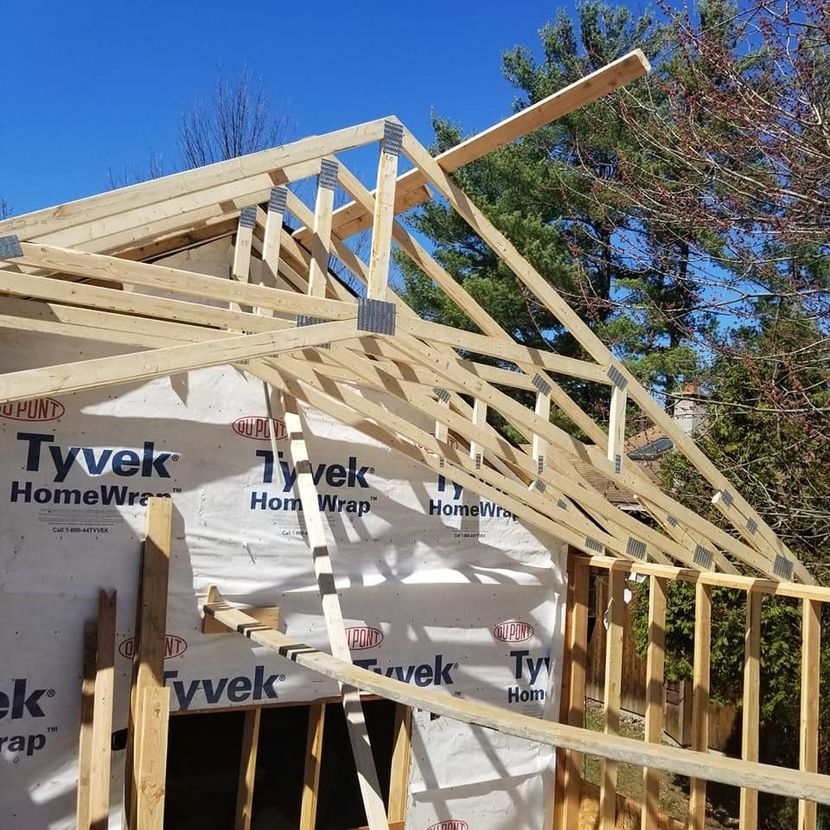 House under construction with exposed wooden roof framing and Tyvek wrap on the walls.