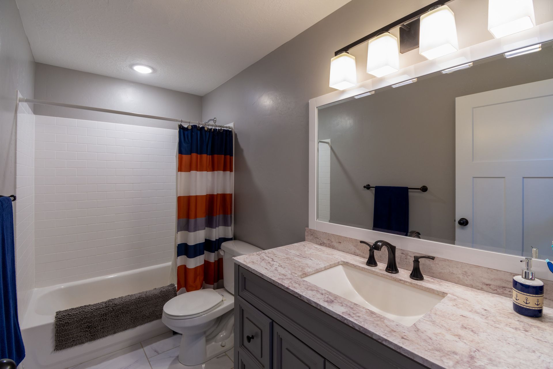 Modern bathroom with white vanity, large mirror, striped shower curtain, and walk-in shower
