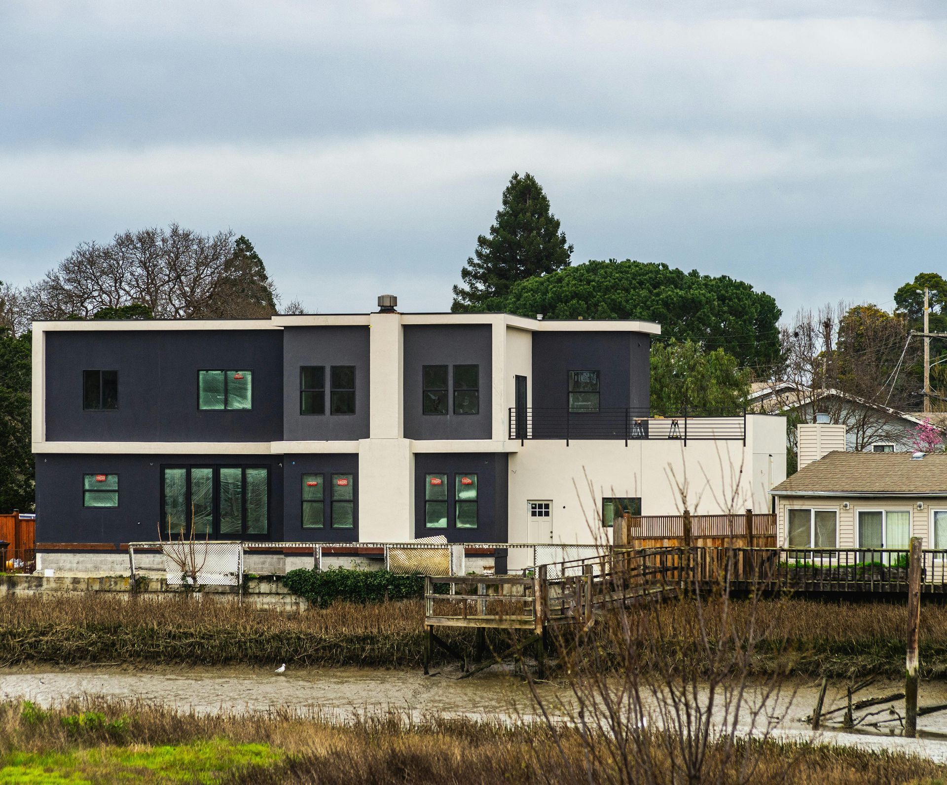 Modern two-story house with dark and white exterior by a canal under an overcast sky