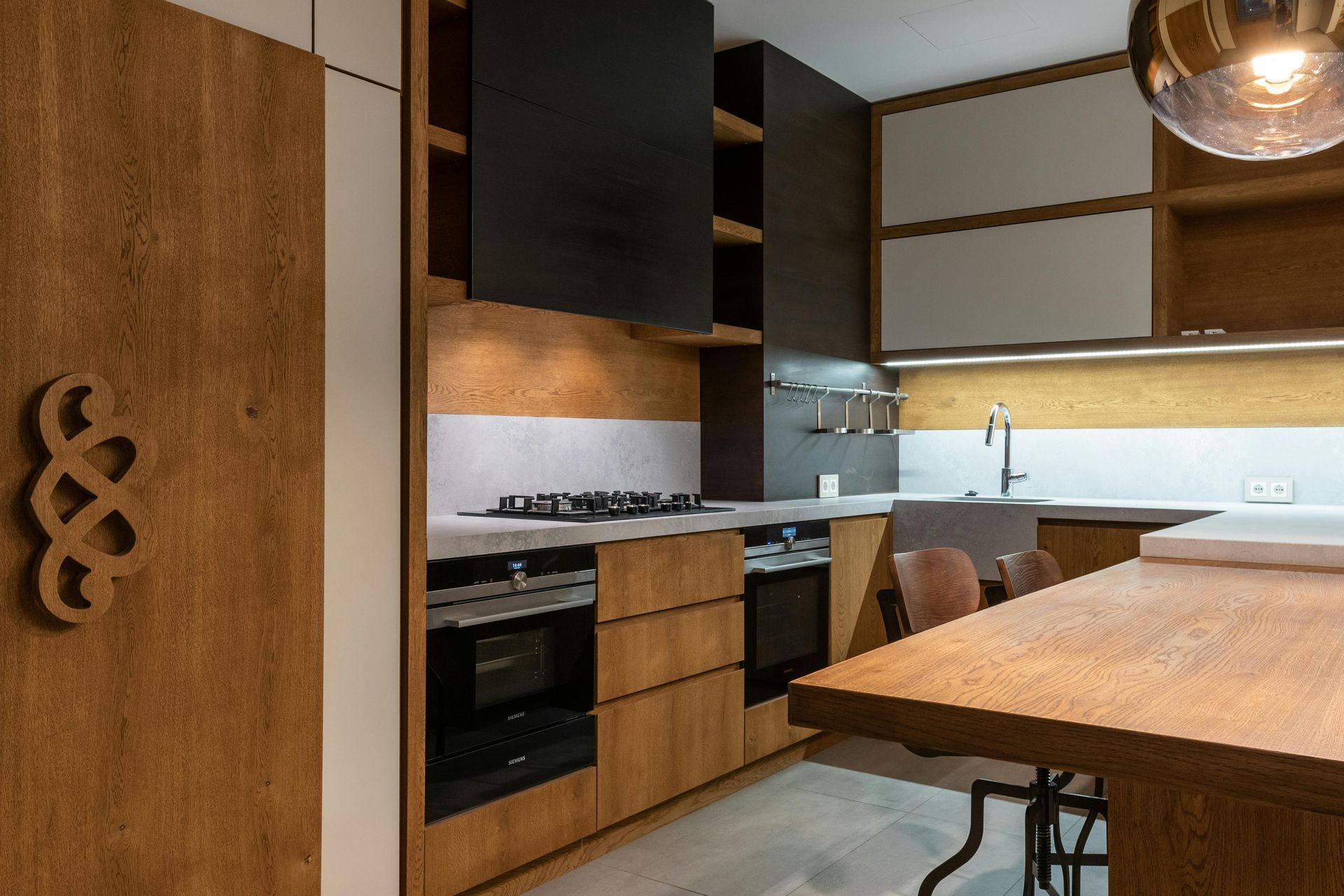 Modern kitchen interior with wood cabinets, black appliances, and a wooden island under warm lighting