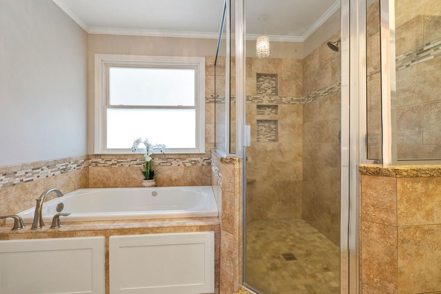 Bathroom with a bathtub, glass shower, beige tile, and window over the tub