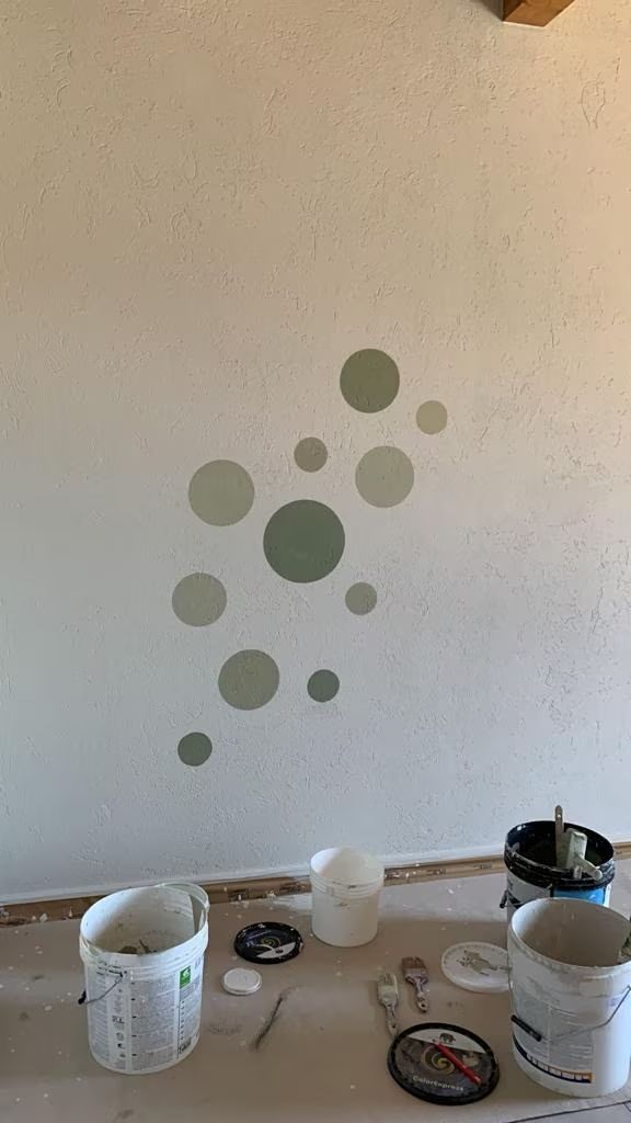 Parete con pois verdi; secchi di vernice e altri materiali sul pavimento.