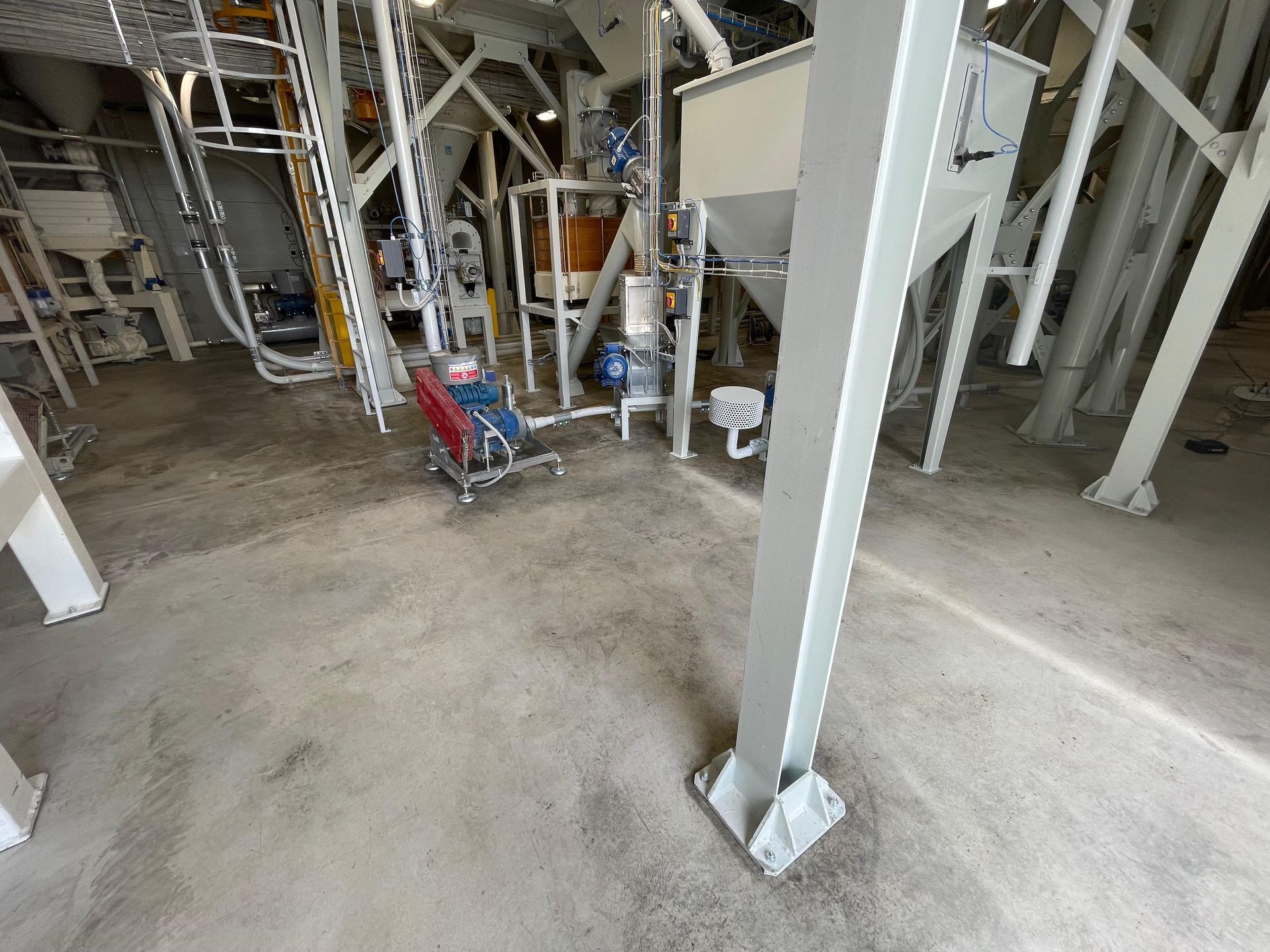 Vista interna del pavimento di una fabbrica con macchinari, tubi e una trave di supporto.