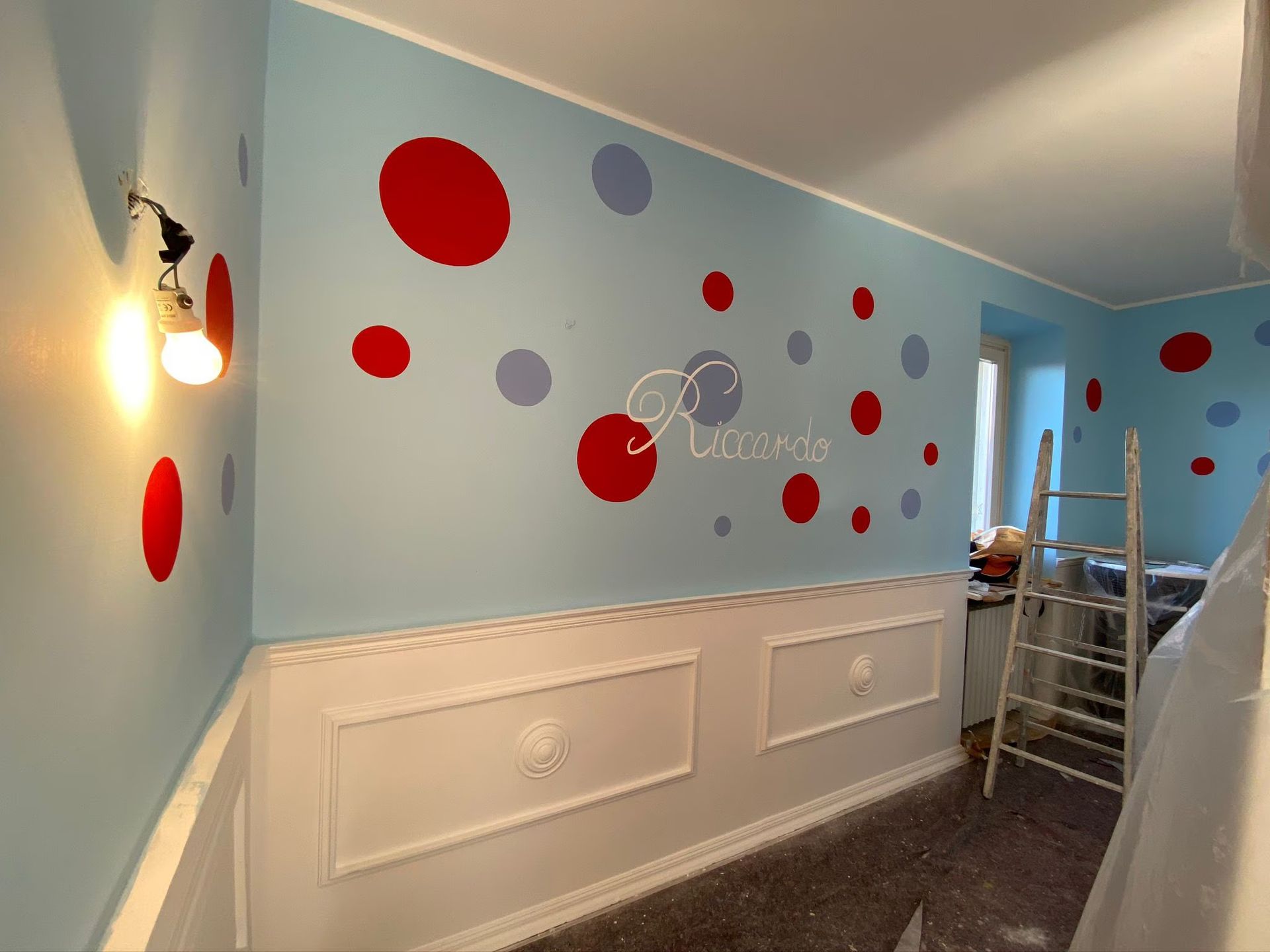Pareti azzurre con pois rossi e grigi, modanature bianche e una scala all'interno di una stanza.