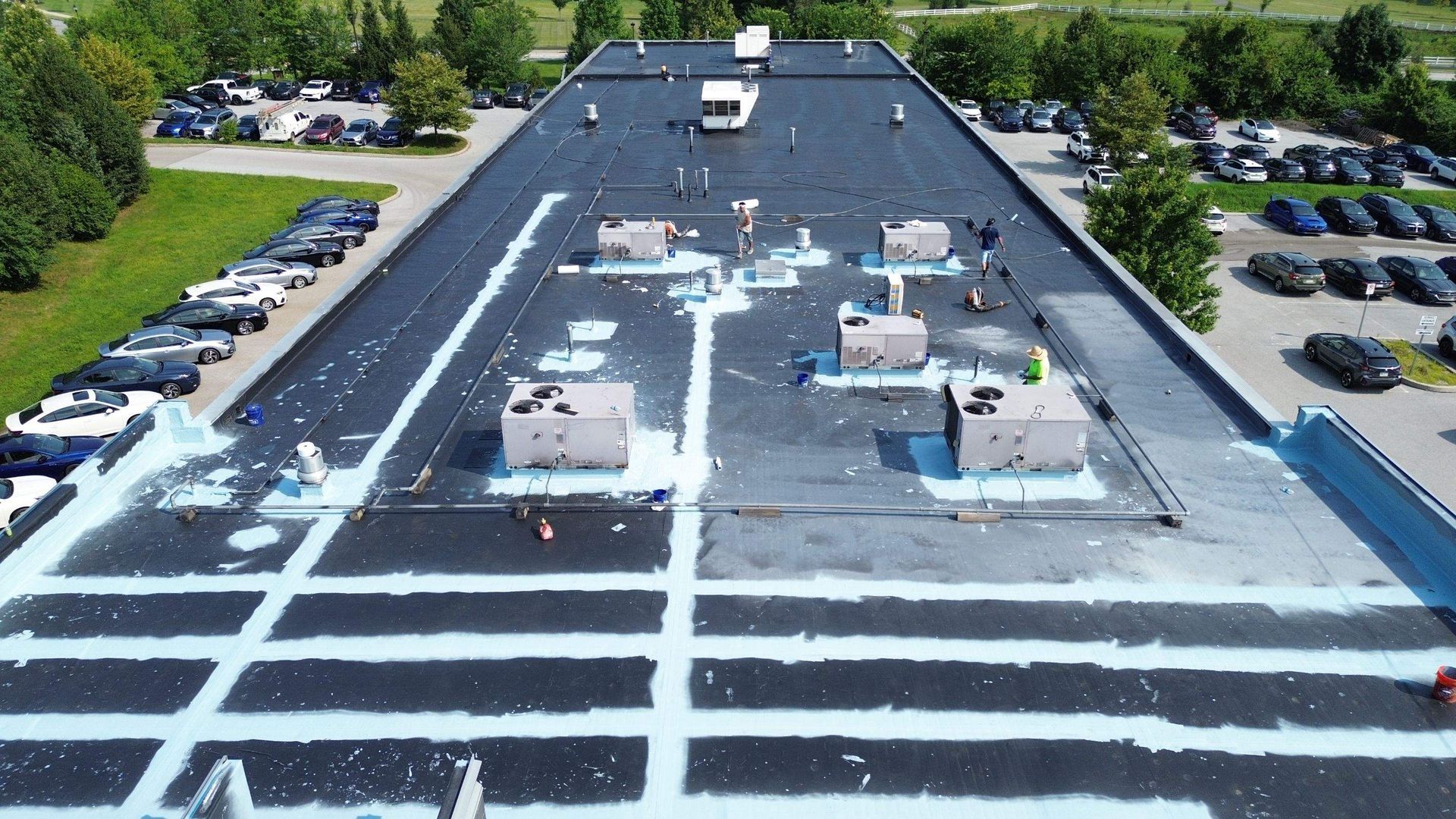 Aerial view of a large, gray metal roof on a commercial building, surrounded by asphalt parking area.