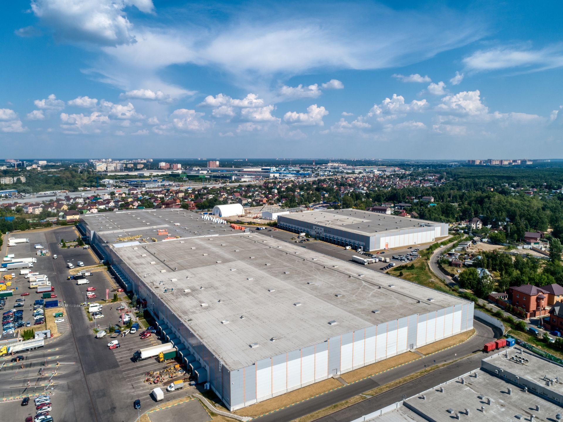An aerial view of large industrial warehouse buildings surrounded by parking lots, roads, and a surrounding town.