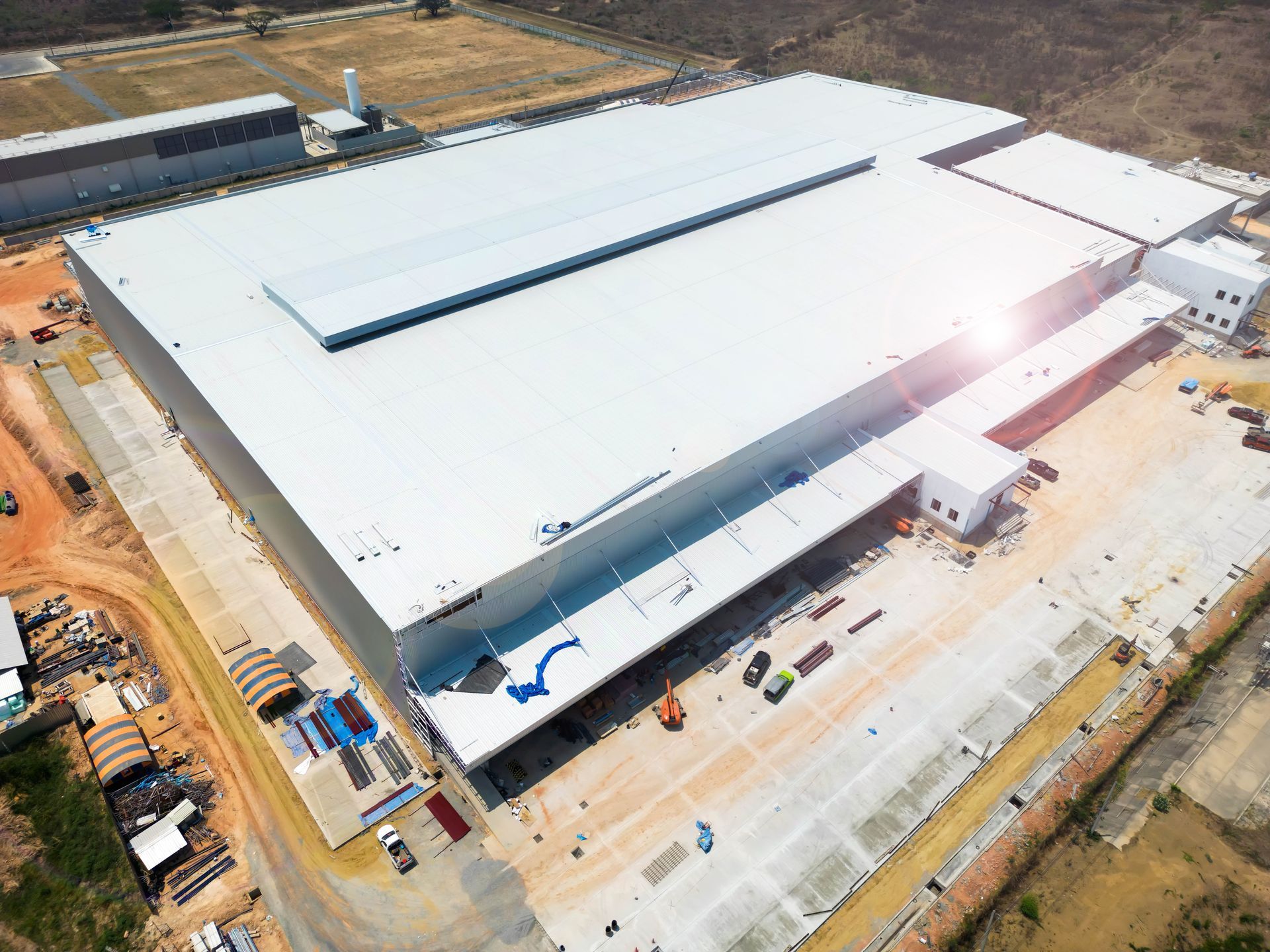 Aerial view of a large white industrial warehouse facility with a flat roof, surrounded by construction and dry land.
