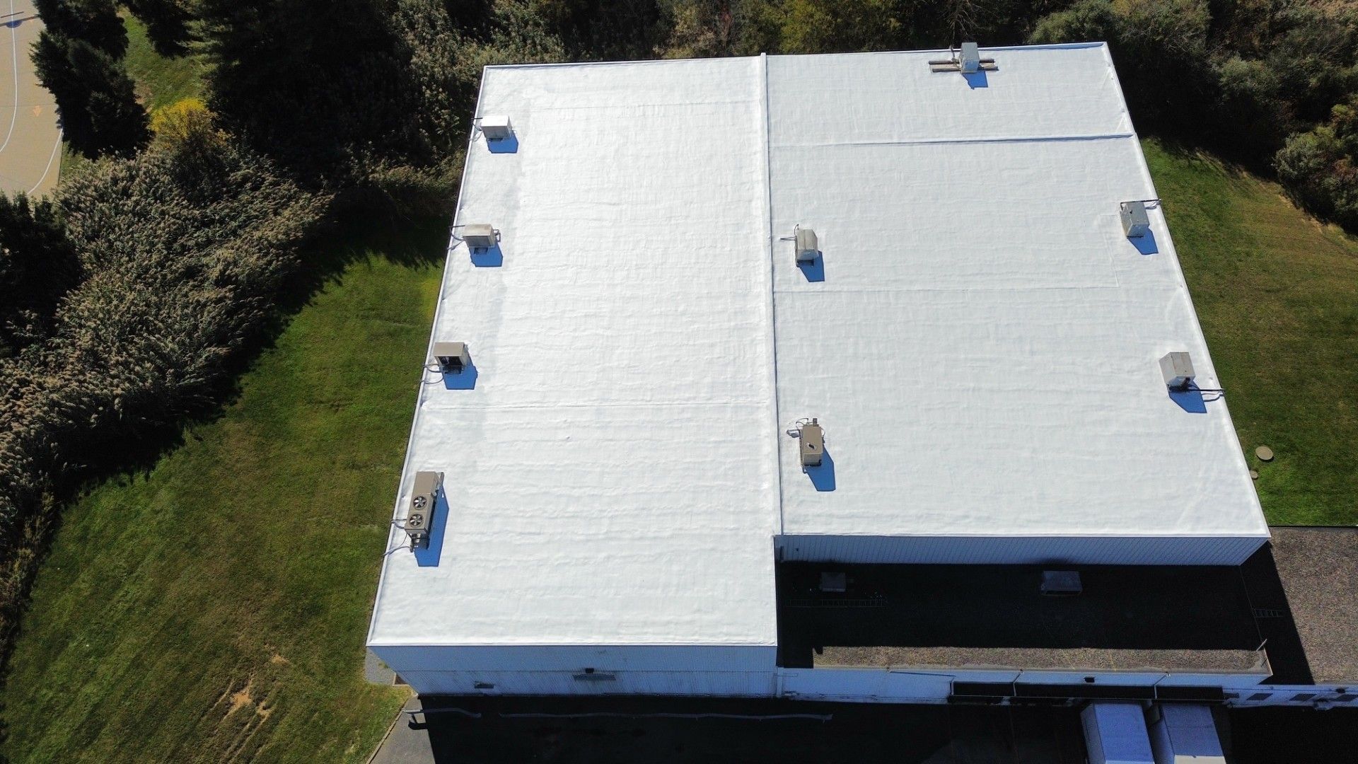 A construction worker in a safety harness and yellow hard hat uses a drill to secure metal roofing panels.
