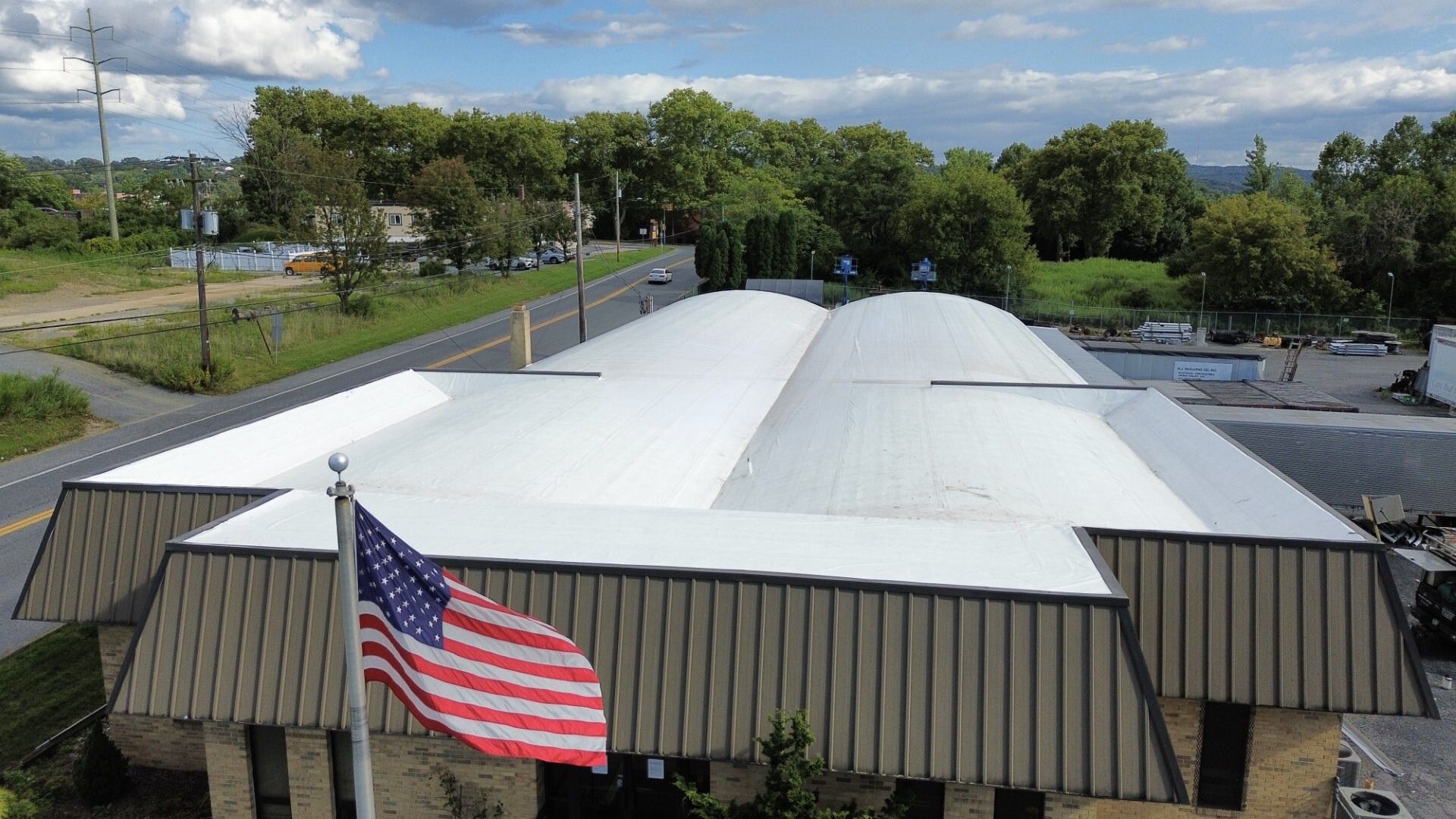 Aerial view of a large commercial building under construction with a steel frame and partially installed white roof.