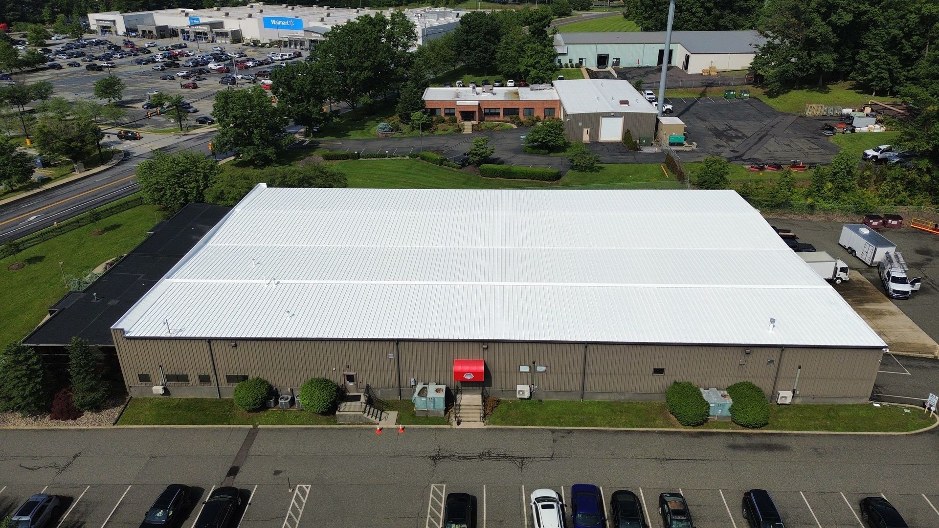 Aerial view of a large, gray metal roof on a commercial building, surrounded by asphalt parking area.