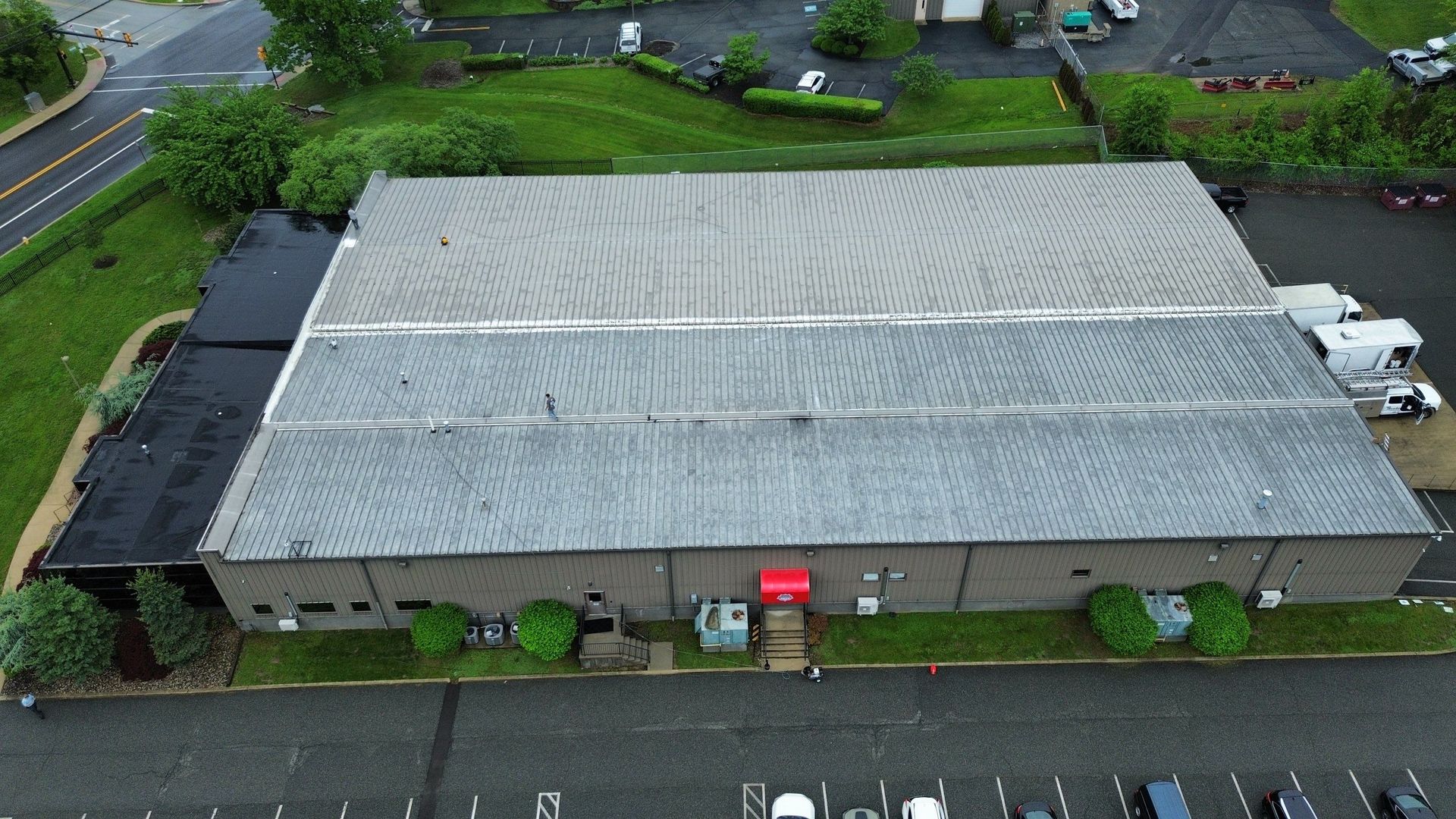 Overhead view of a gray warehouse with a curved metal roof, a yellow tanker truck, and green foliage nearby.