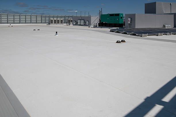 Two construction workers in yellow hard hats and high-visibility vests install metal roofing on a sloped building exterior.