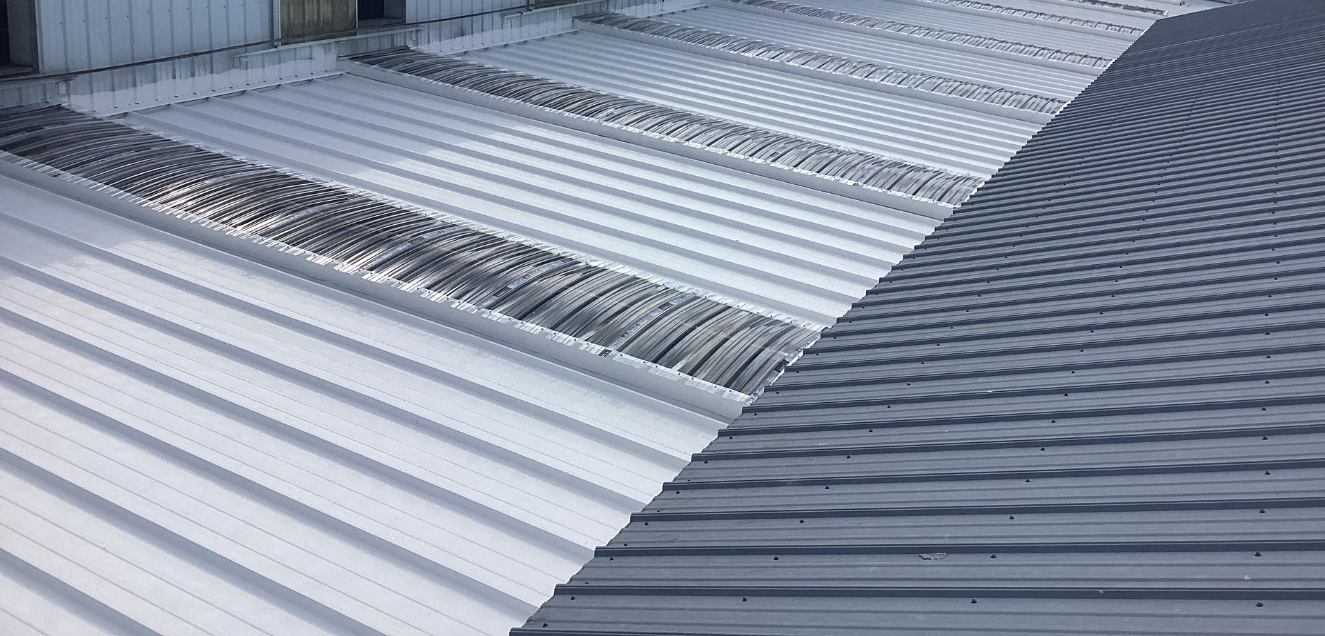 Commercial roofing contractor drills on a red metallic roof tile under the sun.