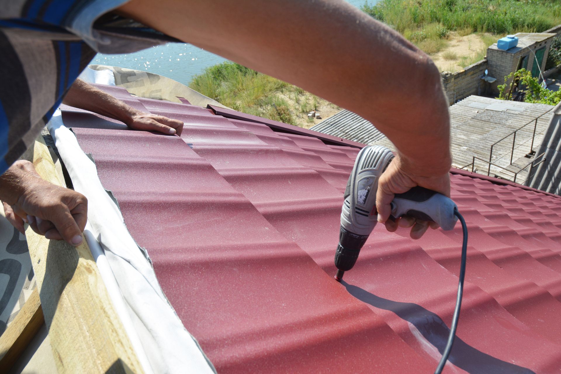Commercial roofing contractor drills on a red metallic roof tile under the sun.
