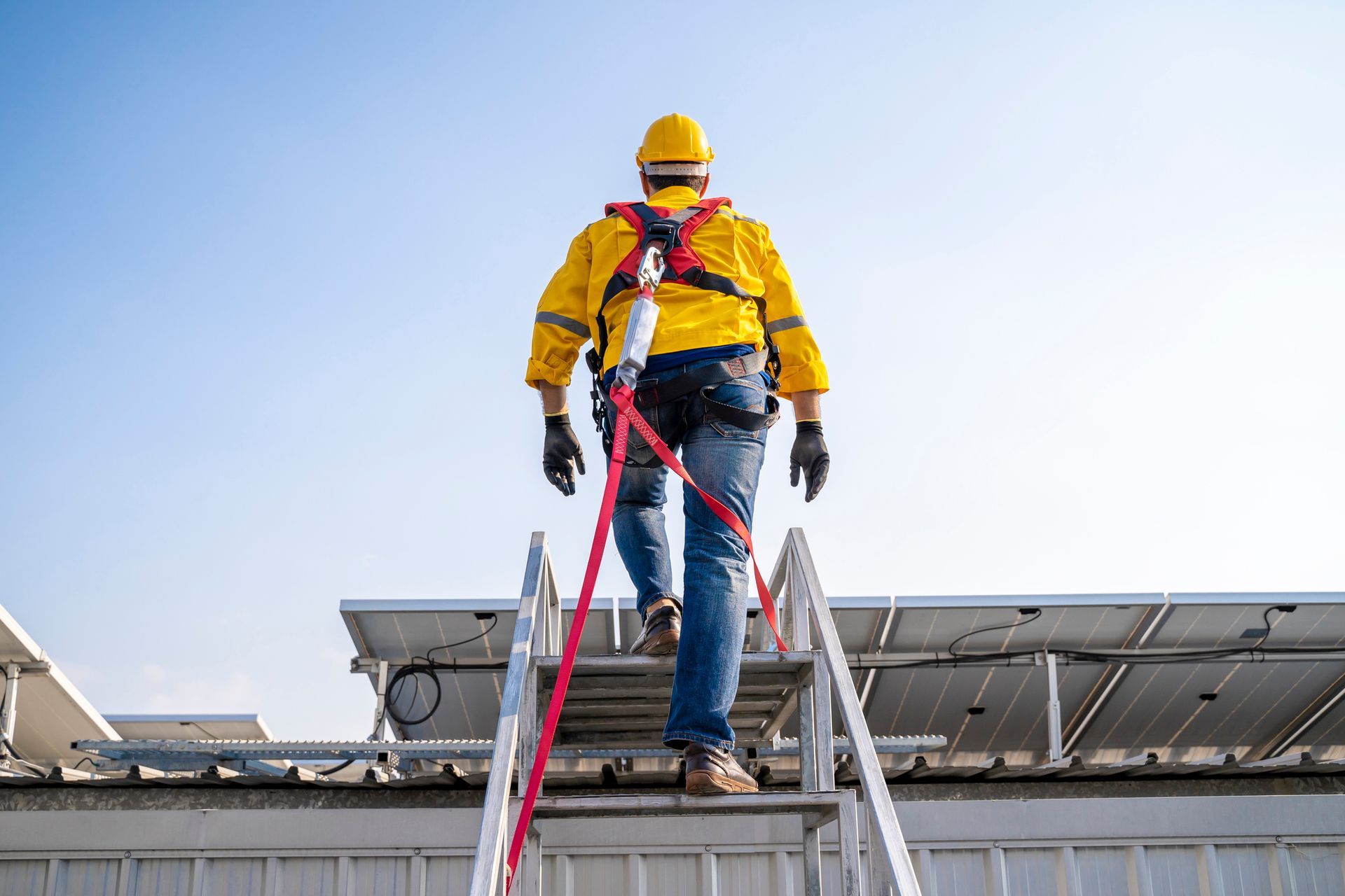Commercial roof repair contractor climbing ladder in safety gear to inspect metal rooftop structure.