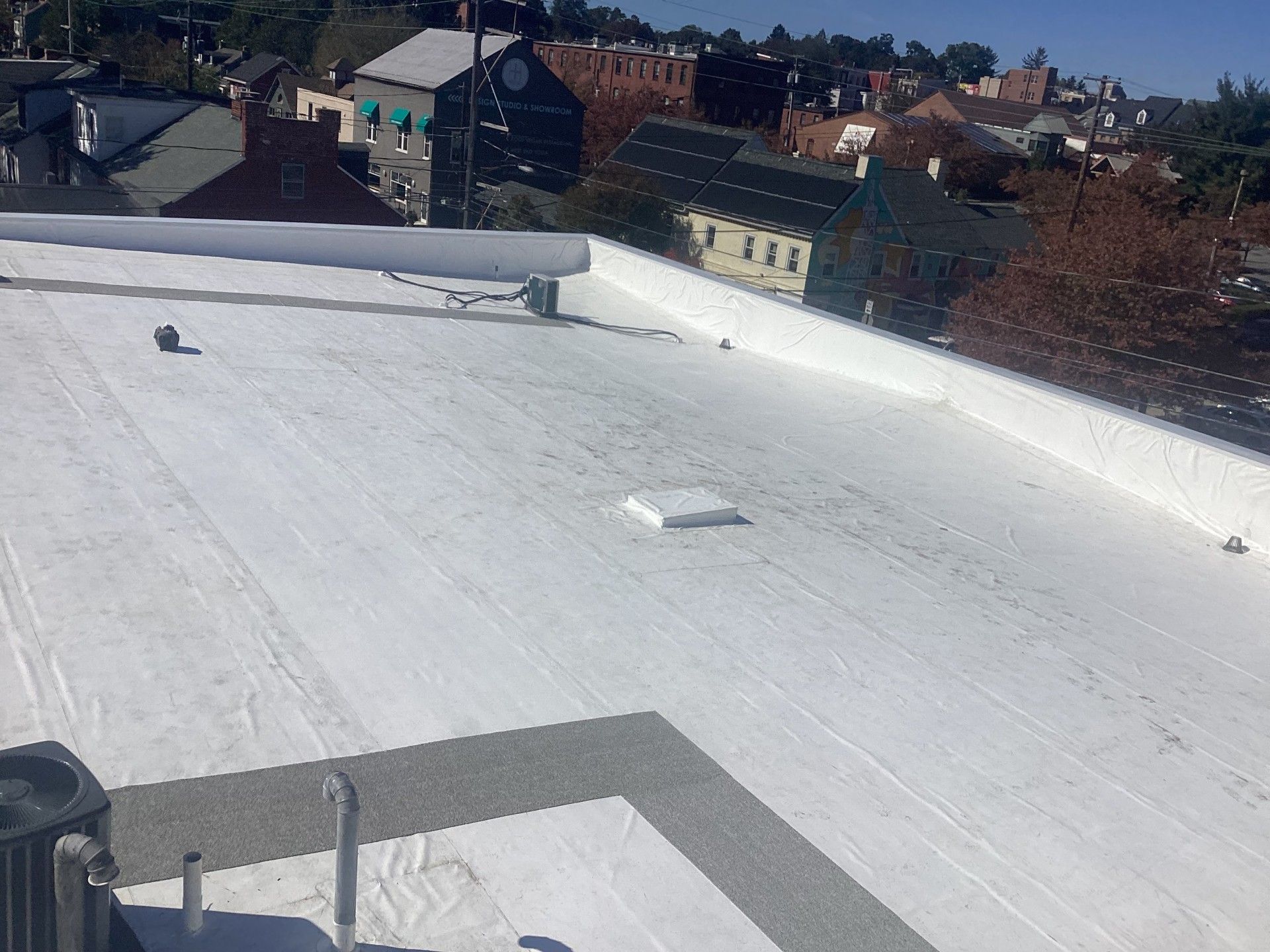 White flat roof with cityscape background. Buildings and trees visible in sunlight.