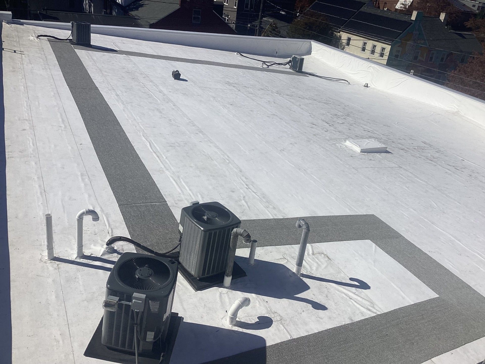 Flat commercial rooftop with HVAC units, white and gray surfaces, sunny day.