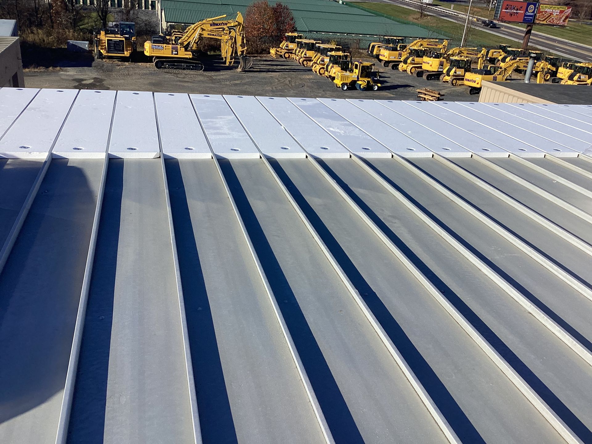 White corrugated metal roof with construction equipment in background.