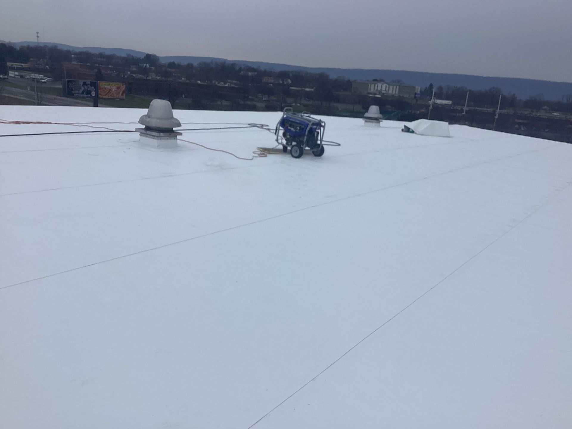 White flat roof with machinery, vents, and a distant cityscape under overcast skies.