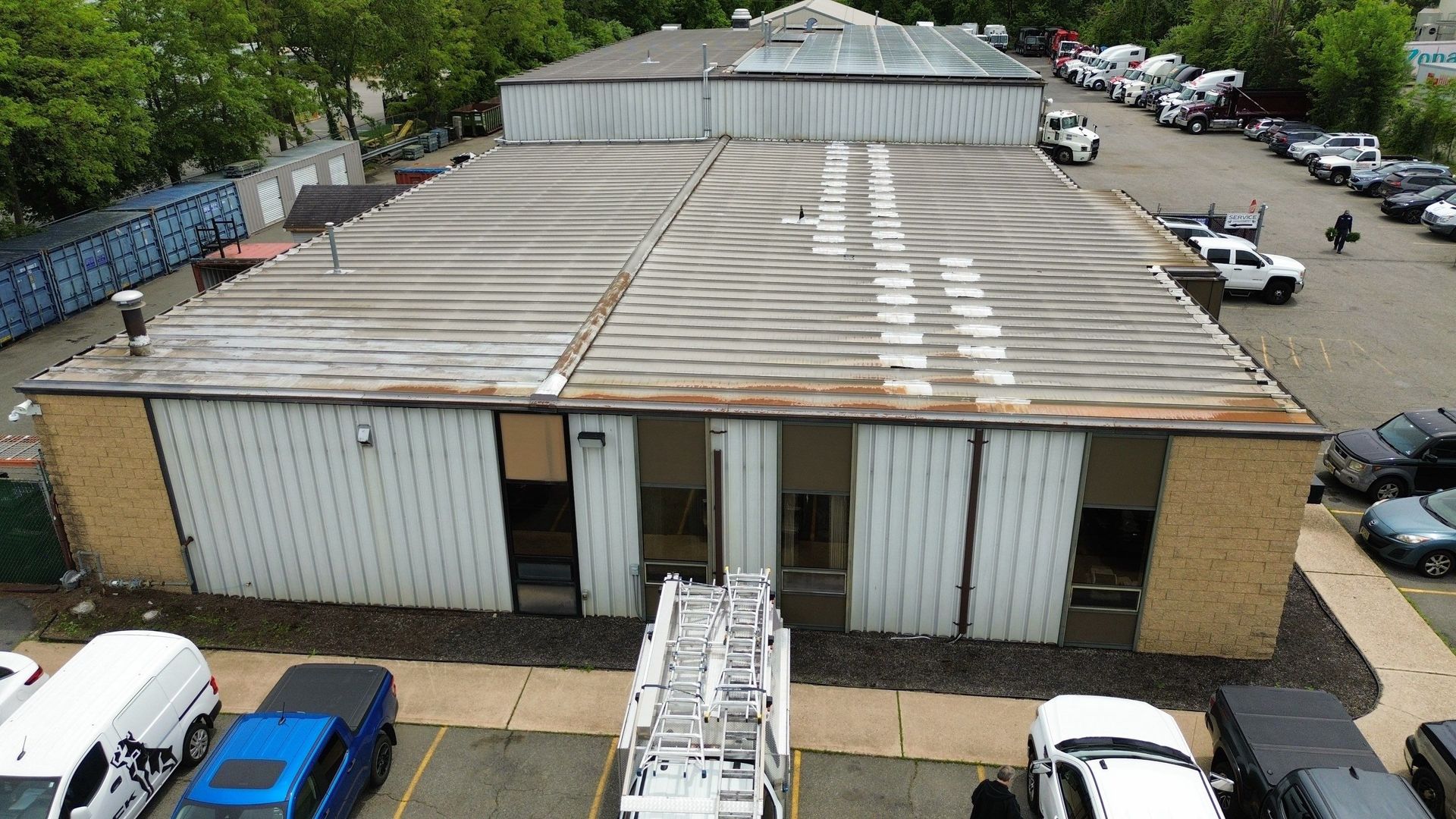 Aerial view of a large, gray metal roof on a commercial building, surrounded by asphalt parking area.