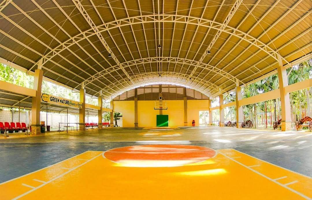 Indoor basketball court, yellow floor, arched roof, concrete columns, basketball hoop at center.