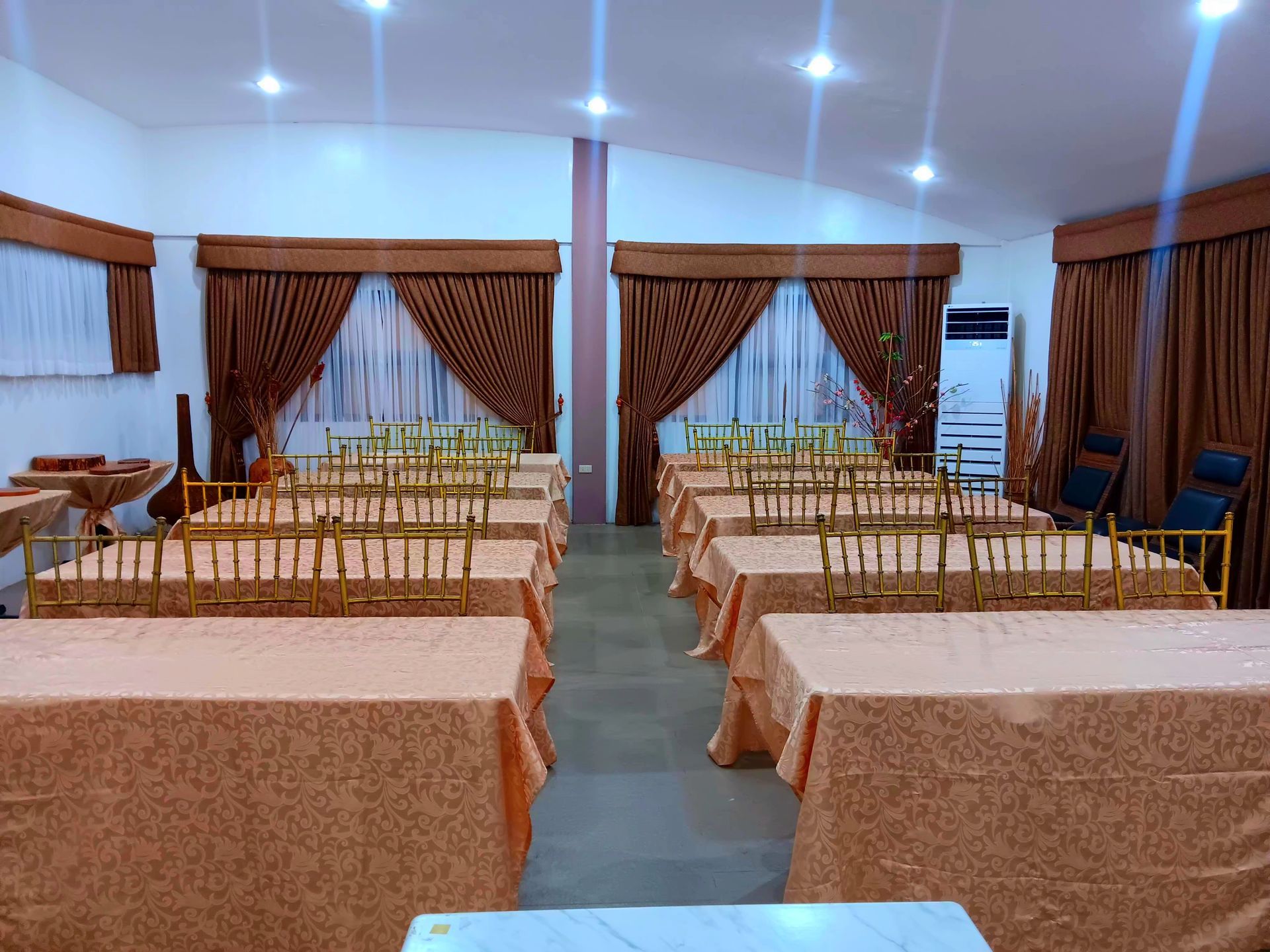 Banquet hall with tables set for a formal event, brown curtains, and gold chairs.