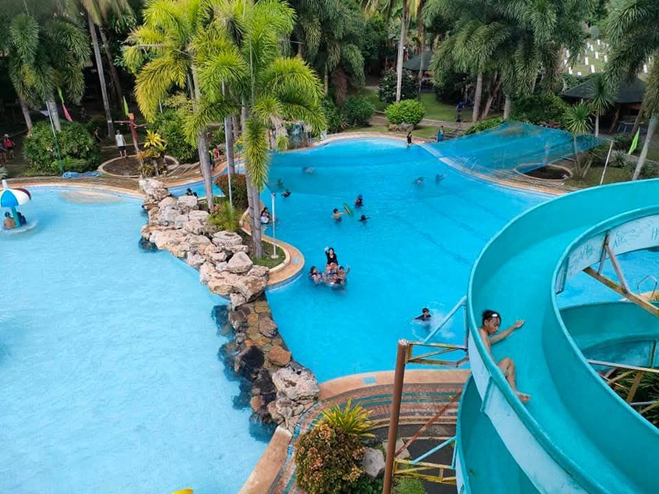 A water park with a blue wave pool, a waterslide, and people enjoying the water in a tropical setting.