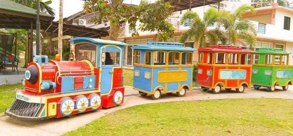 Colorful train with four cars on a grassy path near a building.