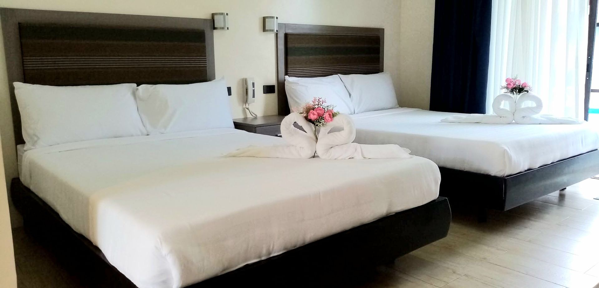 A hotel room with two beds, white sheets, and dark headboards. There are flowers and towel swans on the beds.