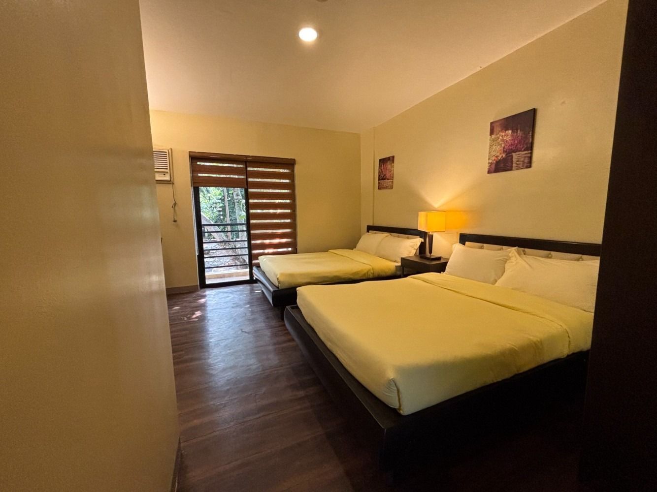Bedroom with two beds, a large one and a smaller one. A glass door leads to a balcony.