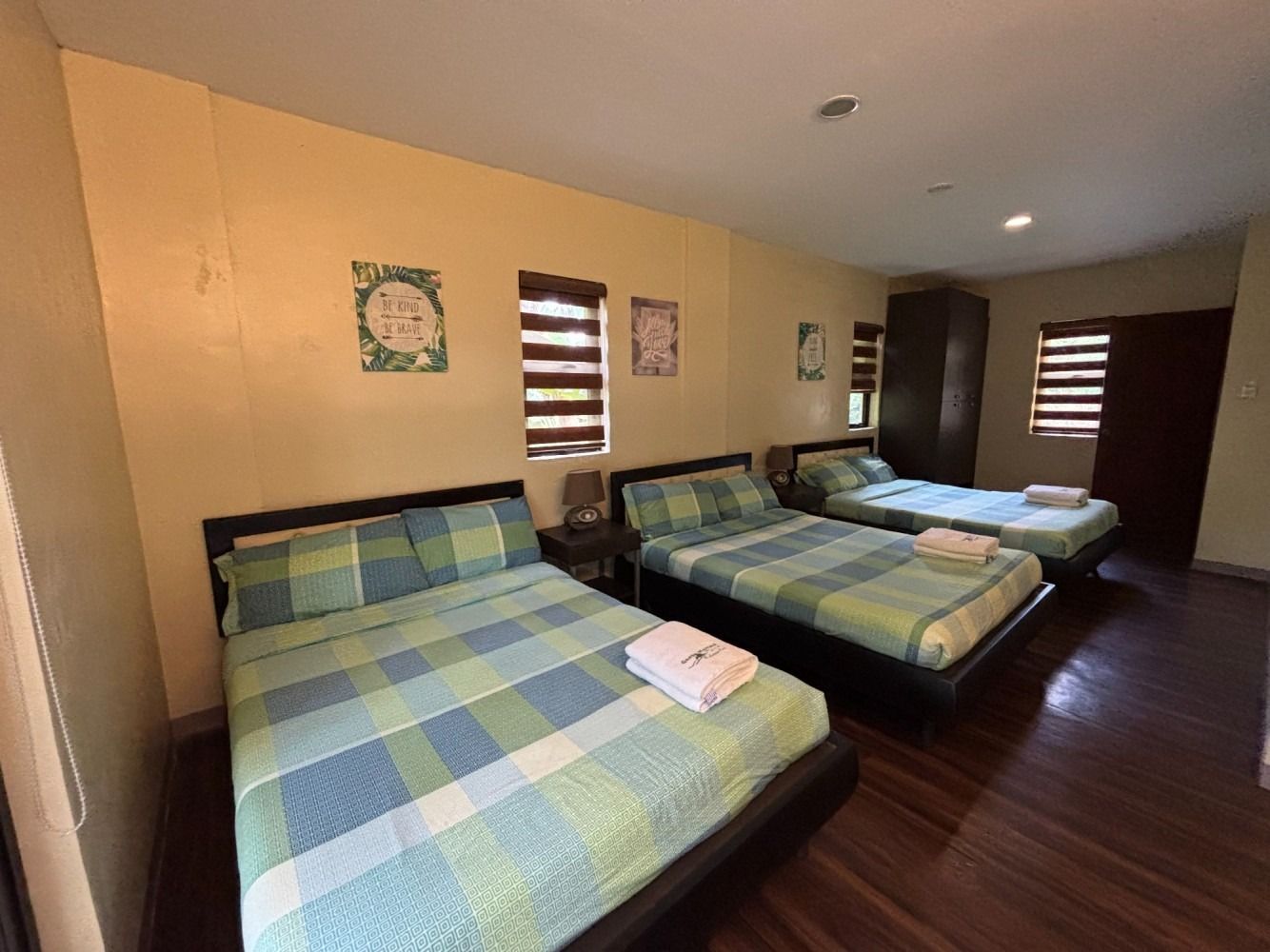 A hotel room with three beds, plaid bedding, and dark wooden furniture.