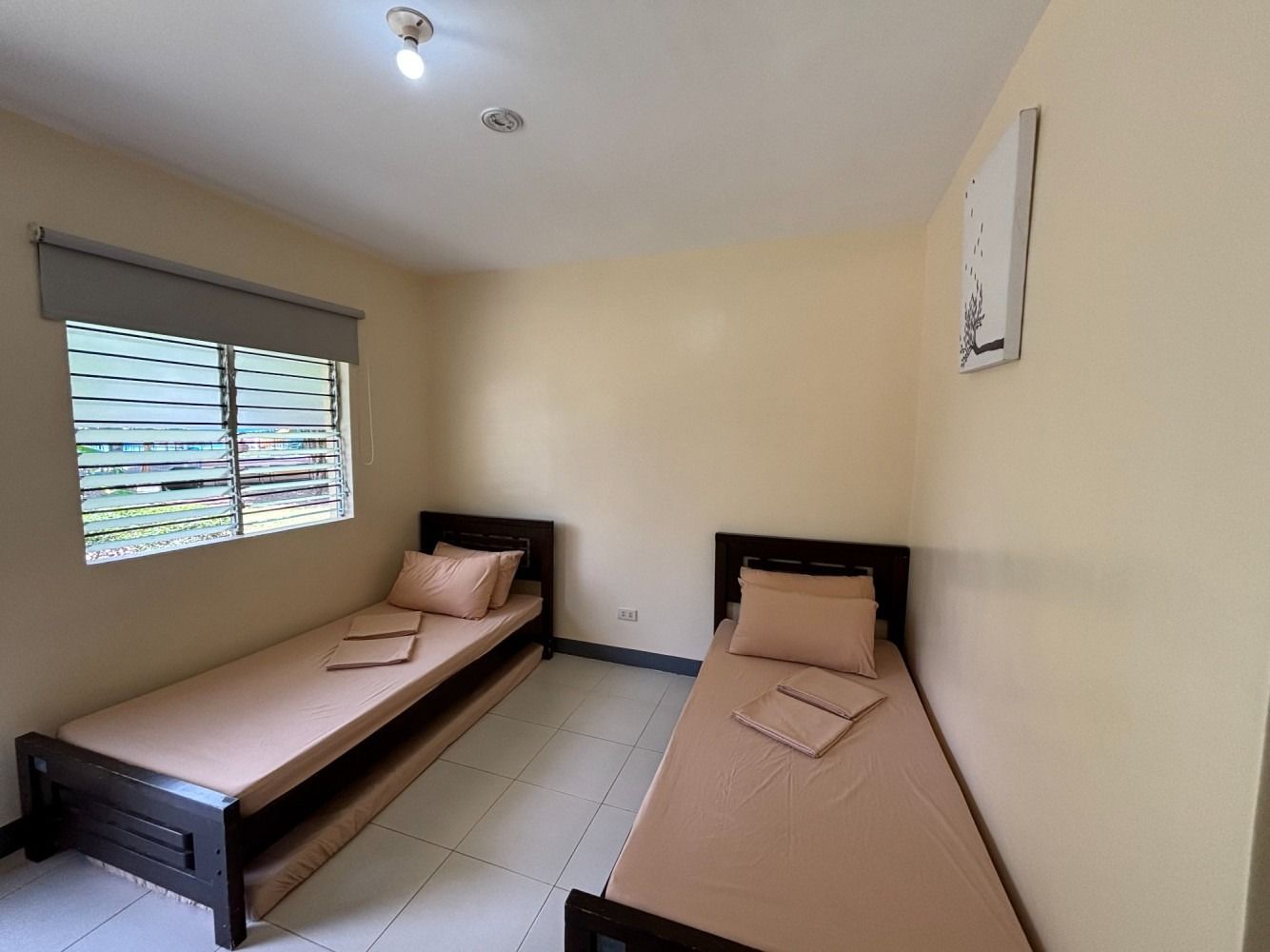 Two single beds in a room with a window, beige sheets and walls, dark wood frames.