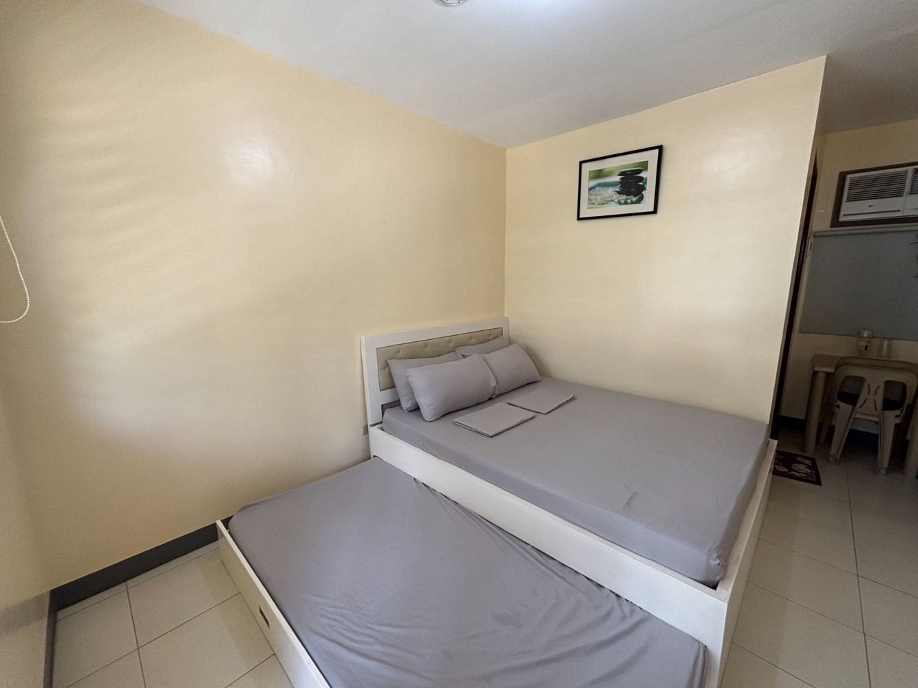 A small room with a double bed and a pull-out bed; beige walls, a picture, and a small table are visible.