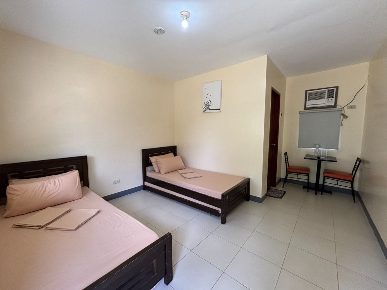 A hotel room with two beds, a small table, and two chairs. Light-colored walls and floors.