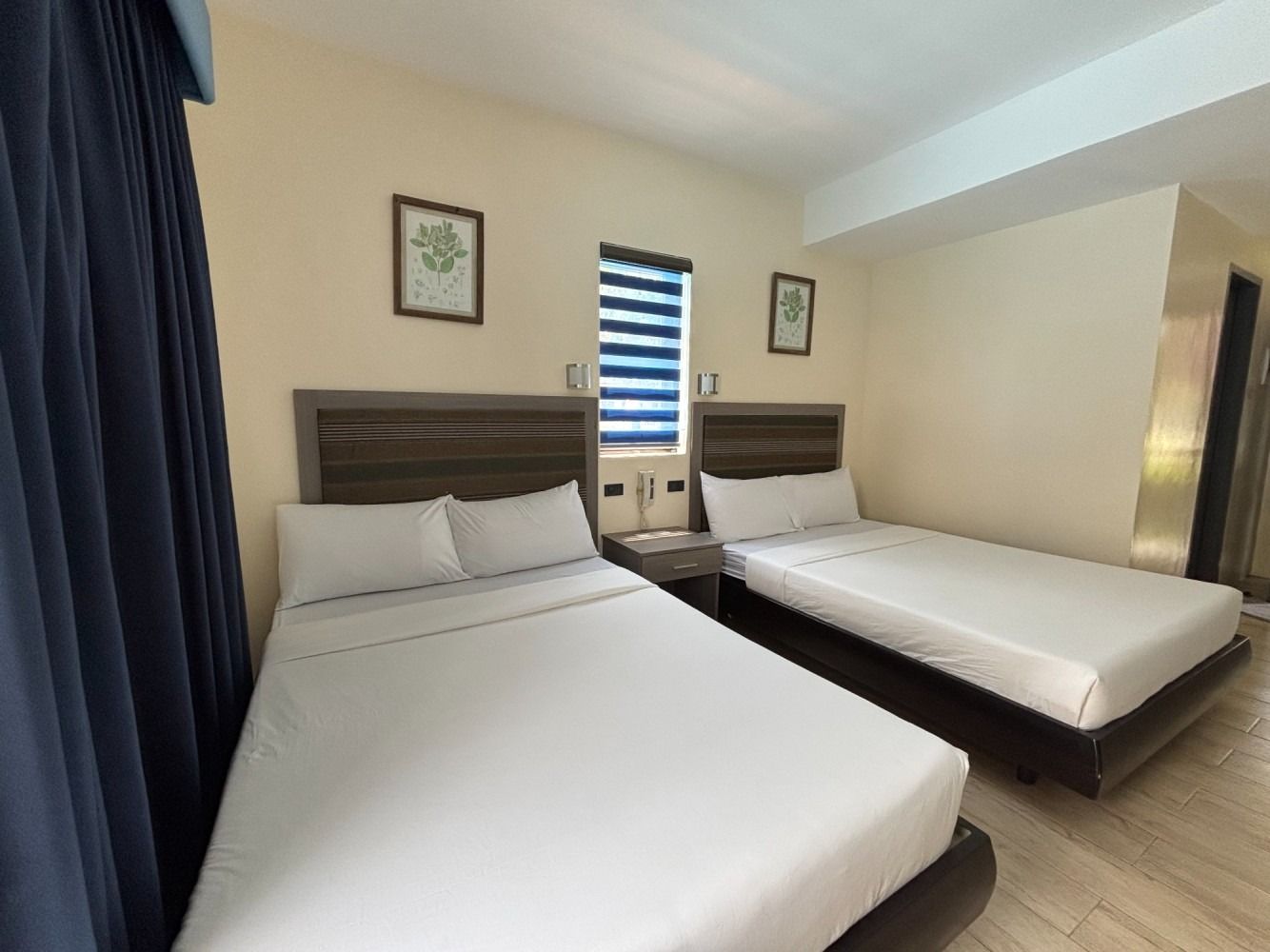 Two beds in a hotel room with white bedding, a small window, and neutral-toned walls.