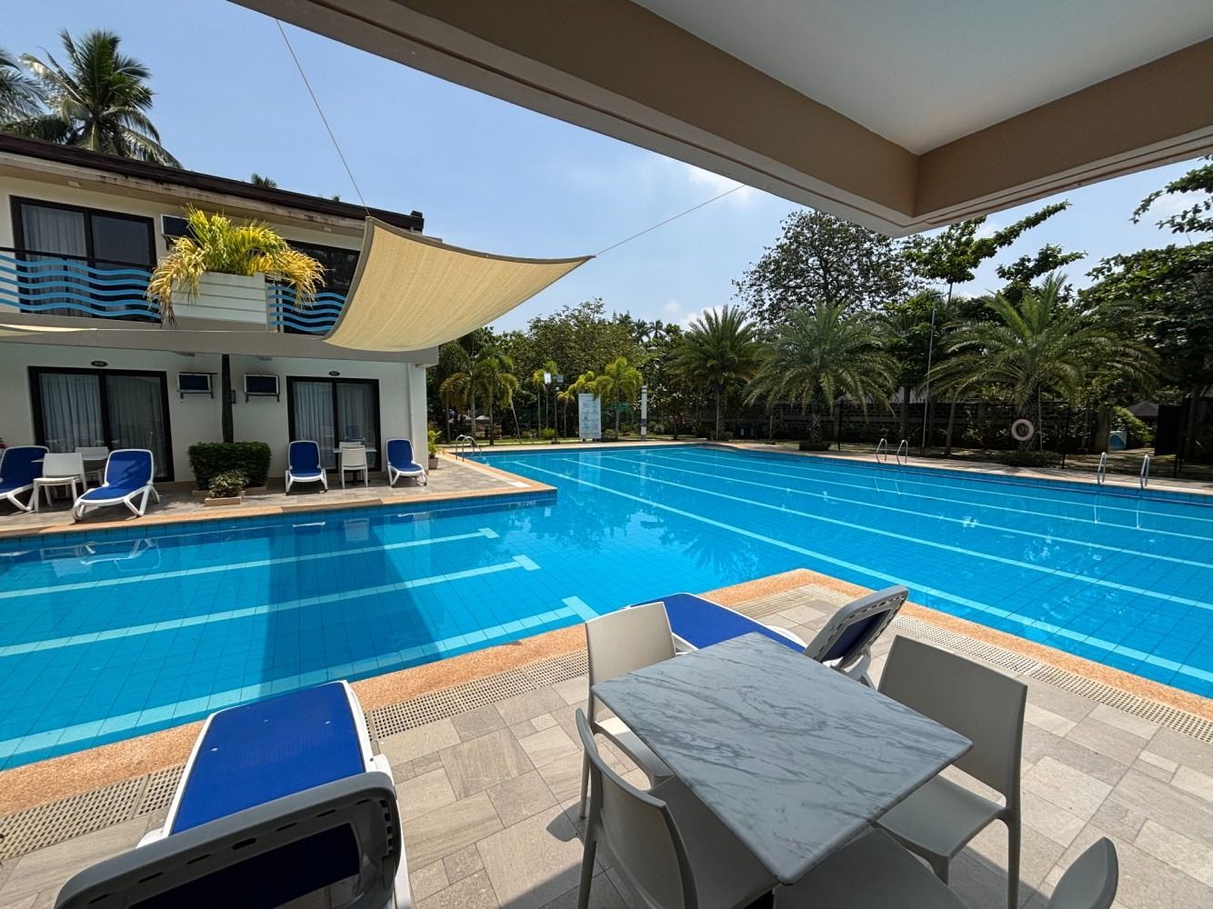 Poolside scene with a pool, seating, and a building under a sunny sky.