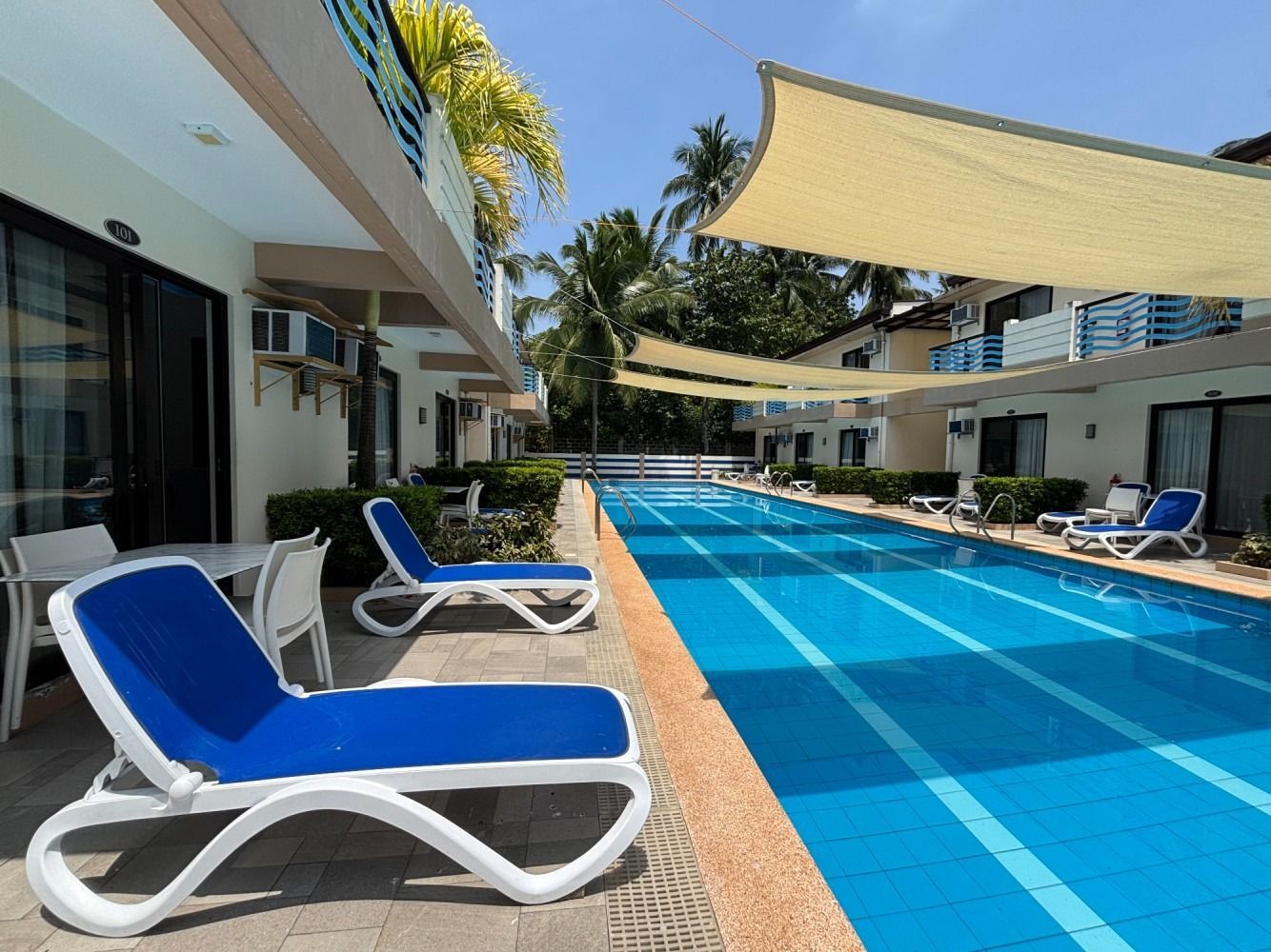 Poolside view of lounge chairs and a swimming pool between two buildings on a sunny day.