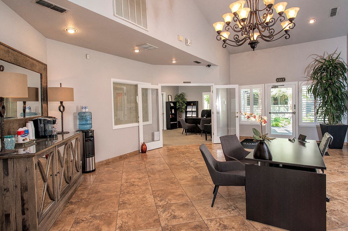 Interior of an apartment community lobby with a reception desk, seating, a water cooler, and glass doors.
