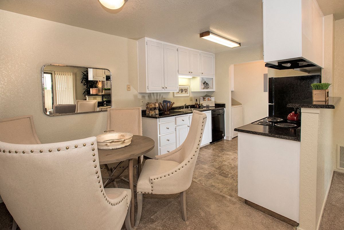 Kitchen and dining area in a beige apartment with white cabinets and a round table with upholstered chairs.