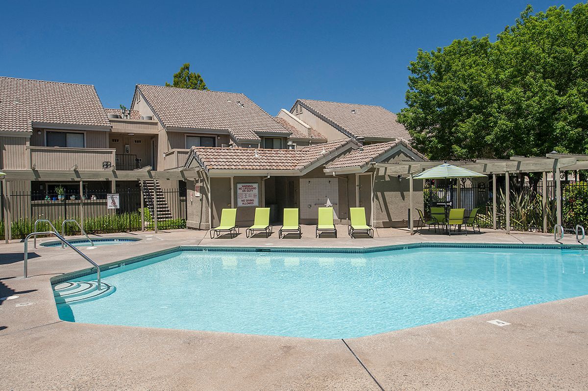 Outdoor apartment community pool with lounge chairs and a shaded seating area.