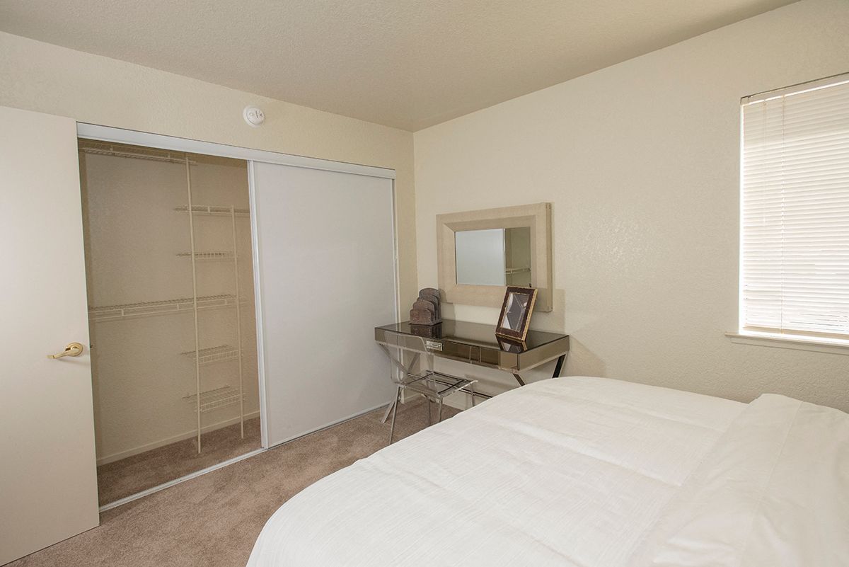 Bedroom in an apartment with a sliding closet door, dresser, mirror, and window blinds.