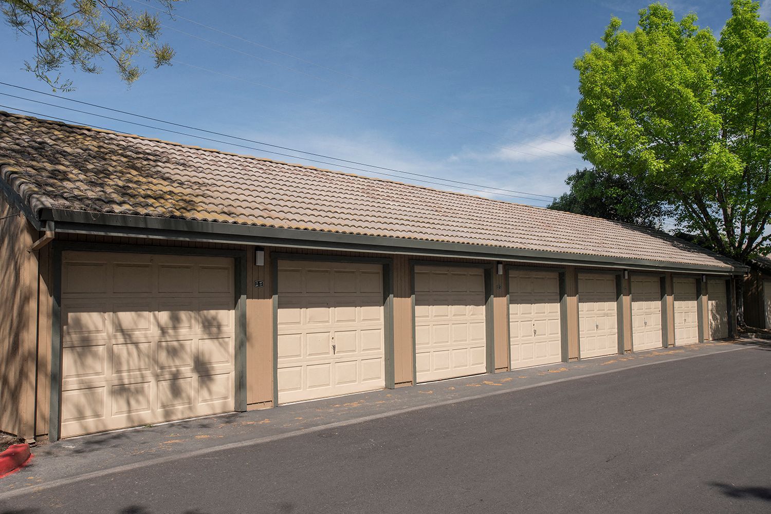 Row of beige garage doors in a single-story building with a tiled roof and trees.