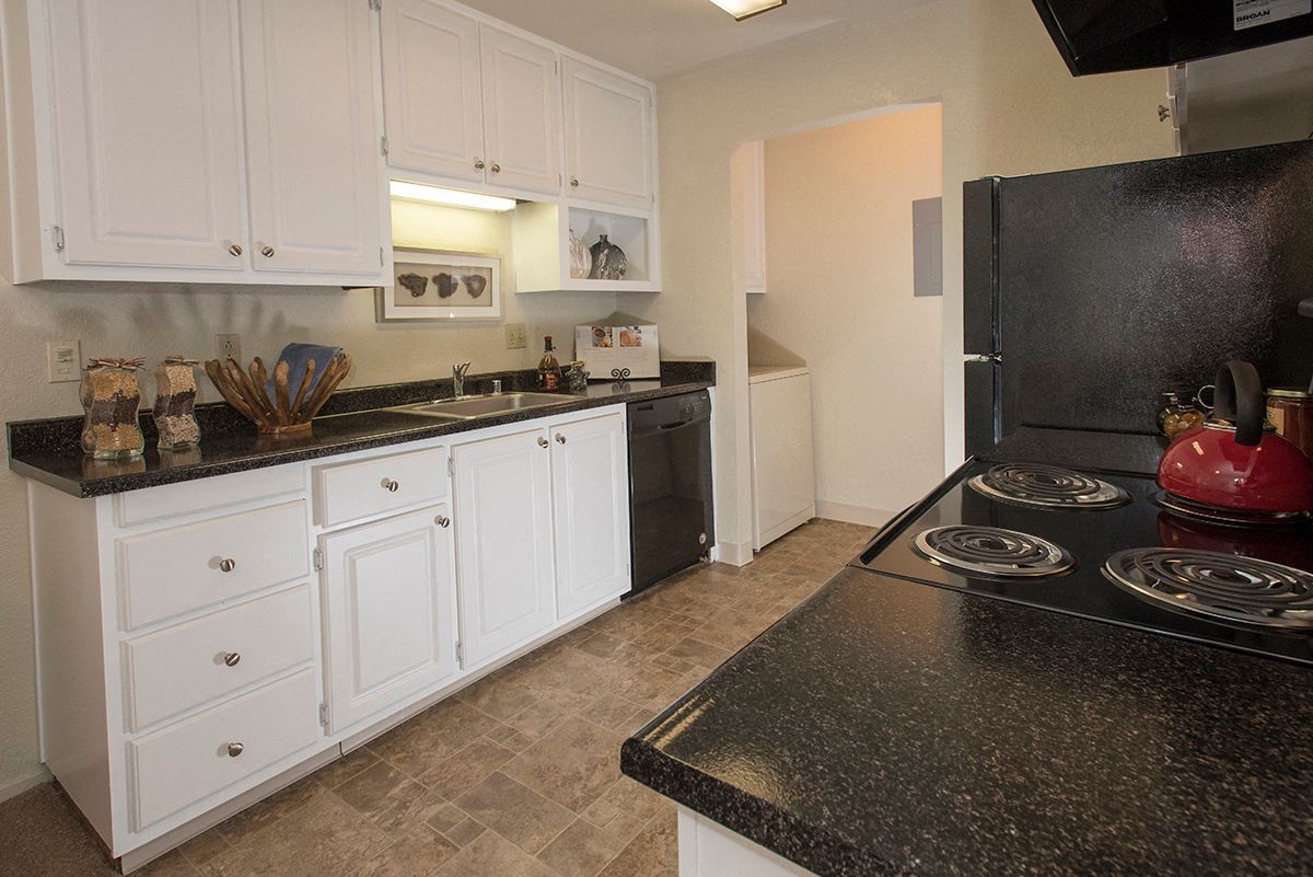 Kitchen with white cabinets, black countertops, and appliances in an apartment unit.