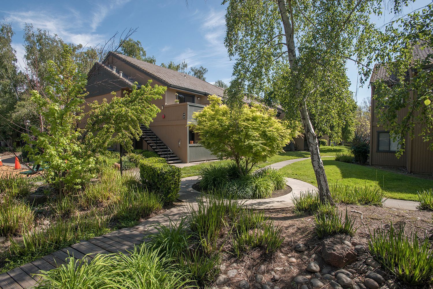 Exterior view of a landscaped apartment community courtyard with a winding path and trees.