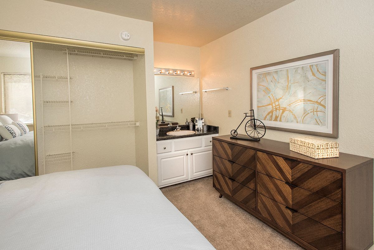 Bedroom in apartment with mirrored sliding closet, vanity, and a wooden dresser.